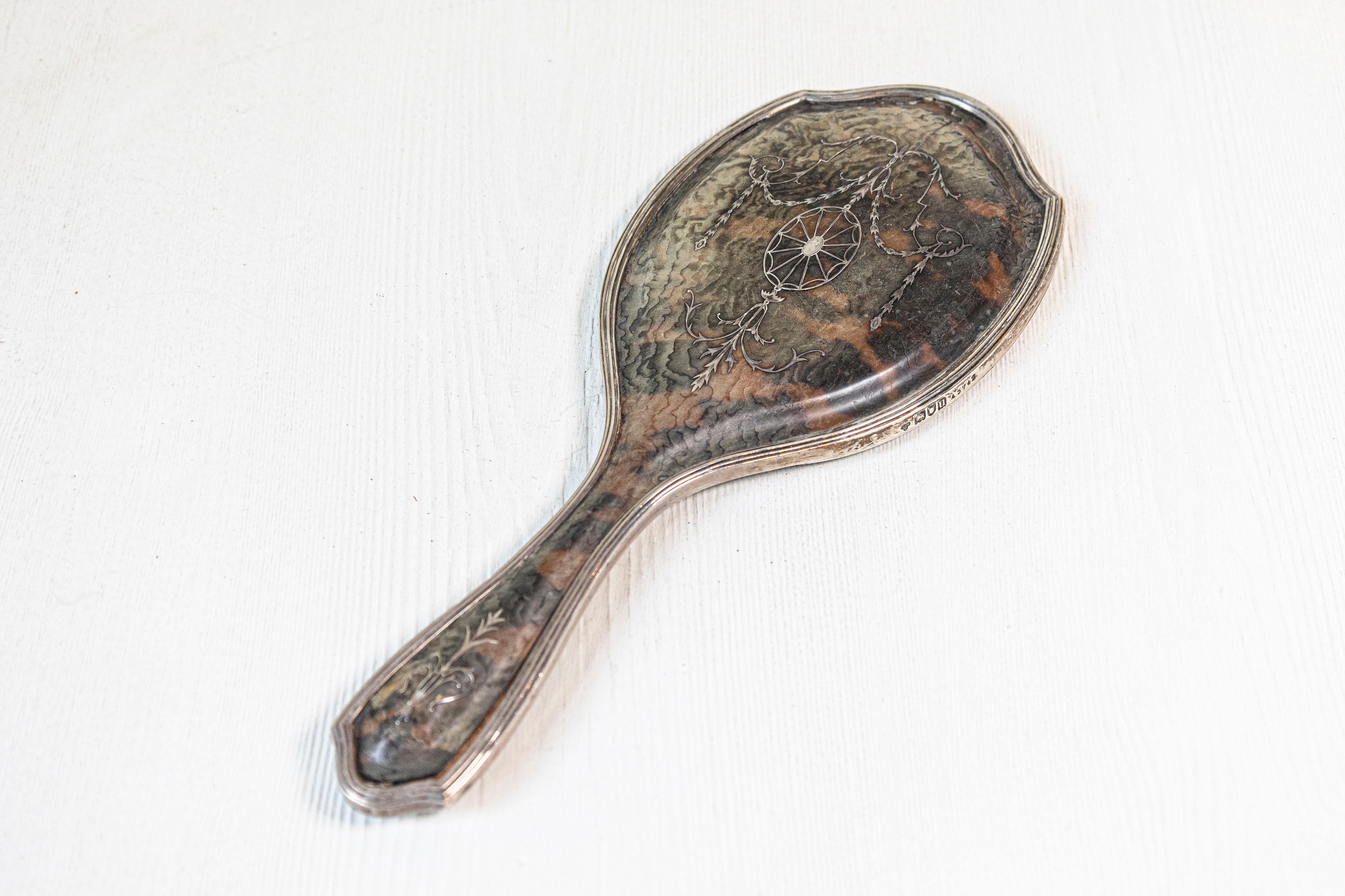 An English silver dressing table hand mirror from the 20th century with silver piqué decor of swags, oval medallion and foliage. Born in England during the 20th century, this exquisite hand mirror features an oval body with arching top, delicately