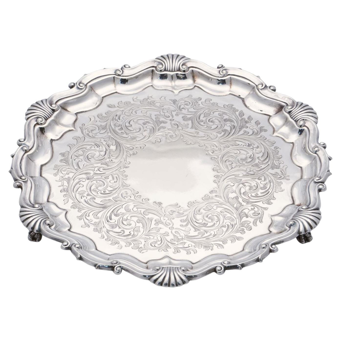 A handsome English round salver or serving or drinks tray of fine plate silver, in the Chippendale style, featuring a pattern of sea shells around the circumference, with an etched scrollwork design in the center.

Impressed mark on back