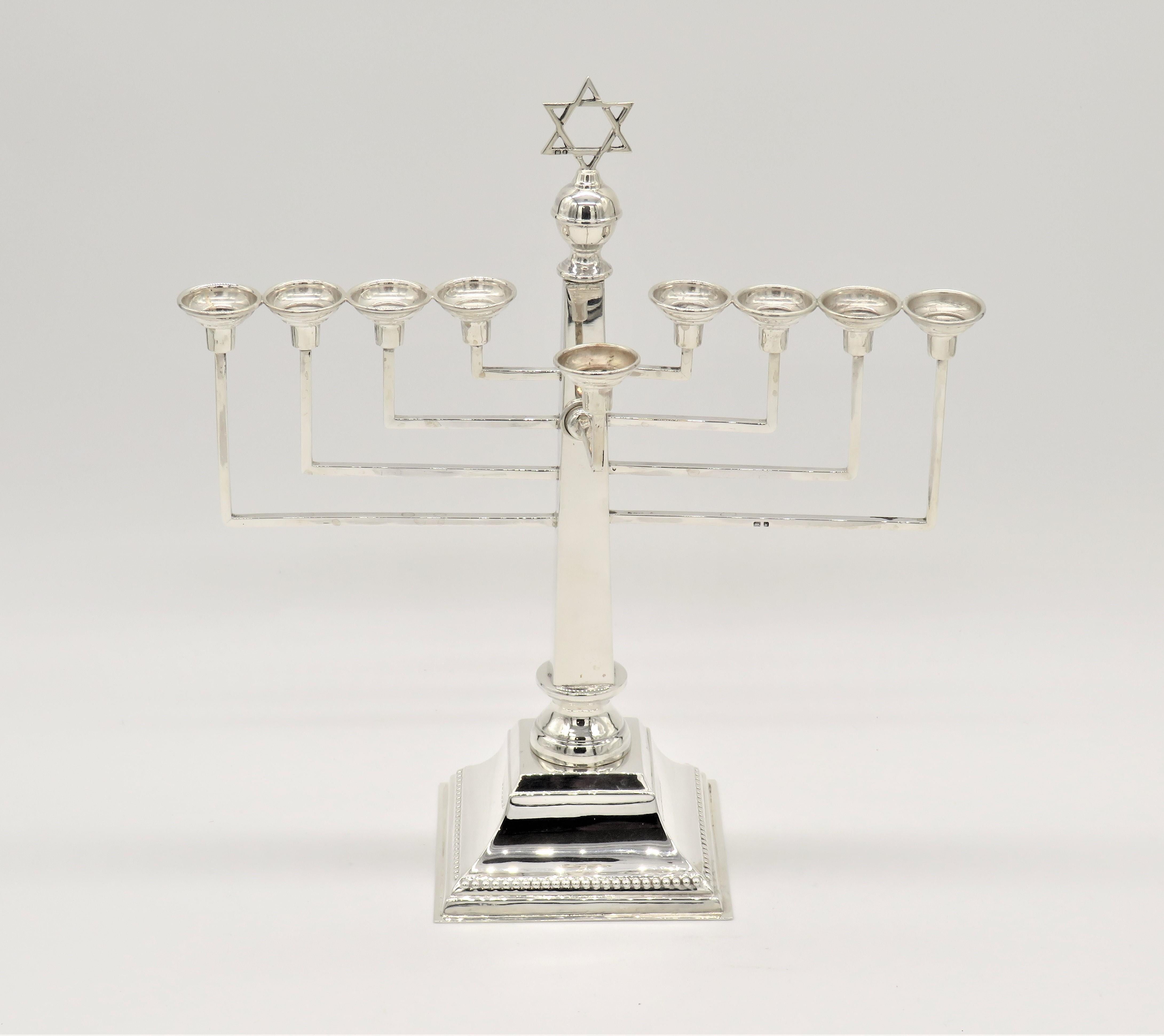 English silver Hanukkah lamp features nine candleholders in traditional style. These round shaped candleholders are supported by tiers of geometric lines. Linear transitions along the surface creates a harmonious visual appearance. In the center