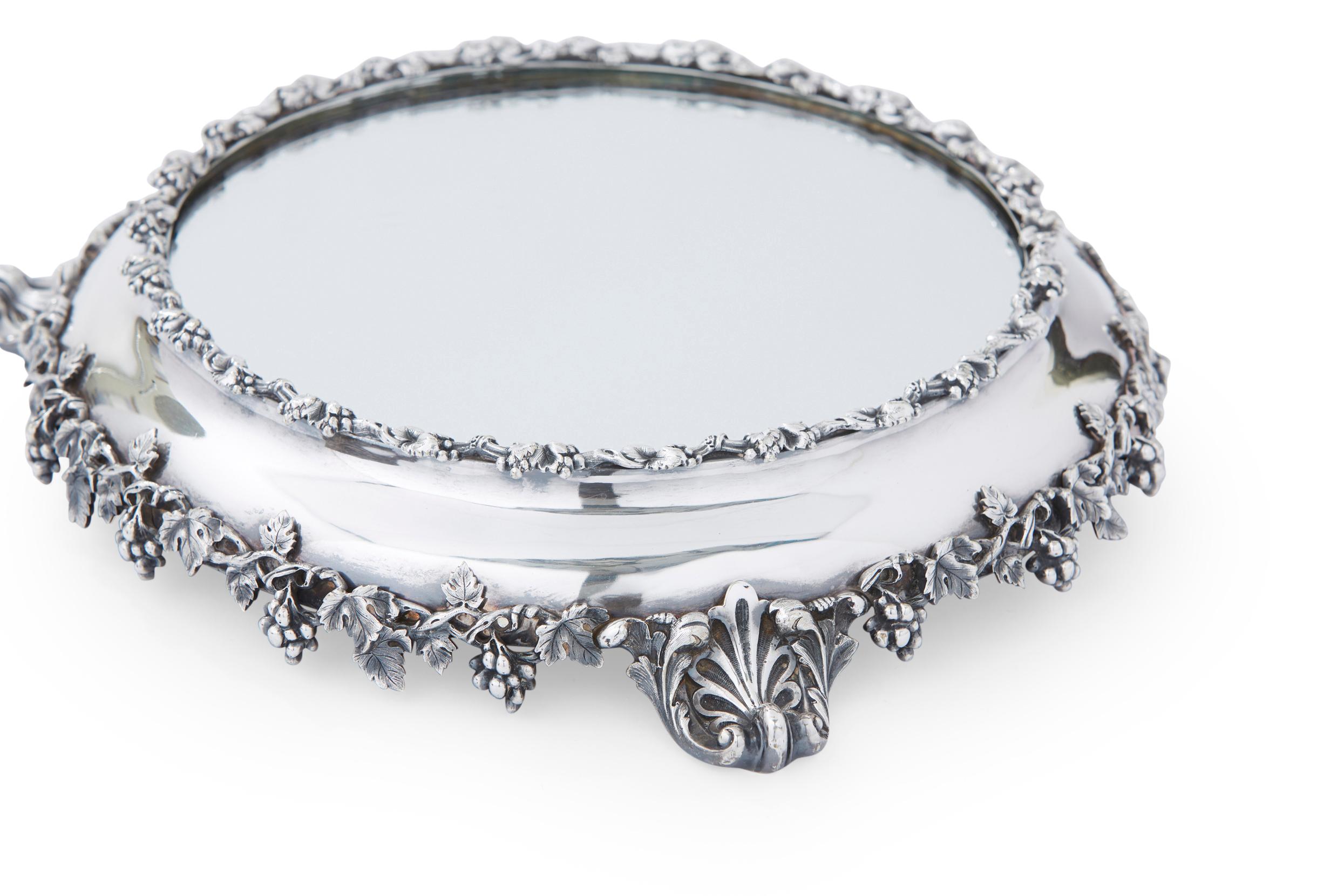 English silver mounted framed mirrored footed vanity tray with exterior floral design details. The mirrored vanity tray is in great antique condition. Minor wear consistent with age / use. The tray stands about 15 1/2 inches diameter x 3 inches high.