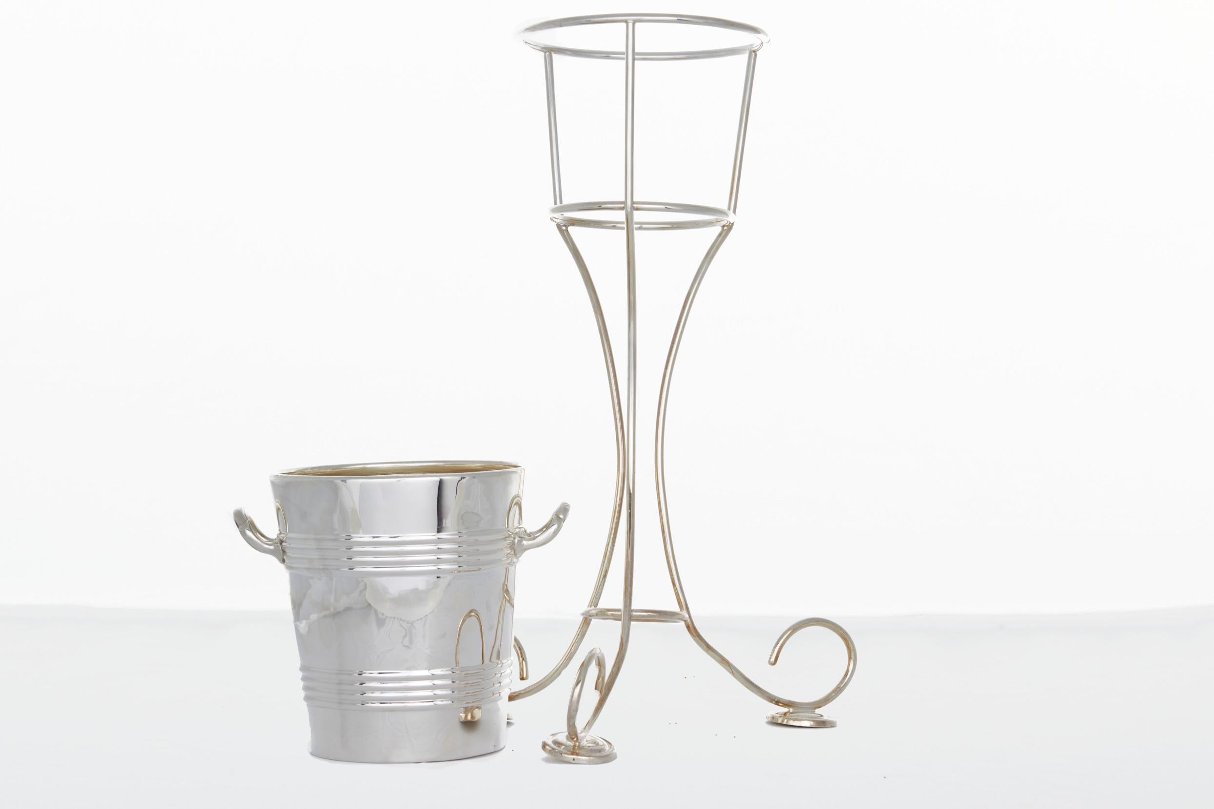 Mid 20th Century English barware / tableware Silver plated champagne bucket / wine cooler on stand . The Wine cooler / ice bucket features an arts & craft style with two side handles . The piece is in good condition . Minor wear . The holding stand