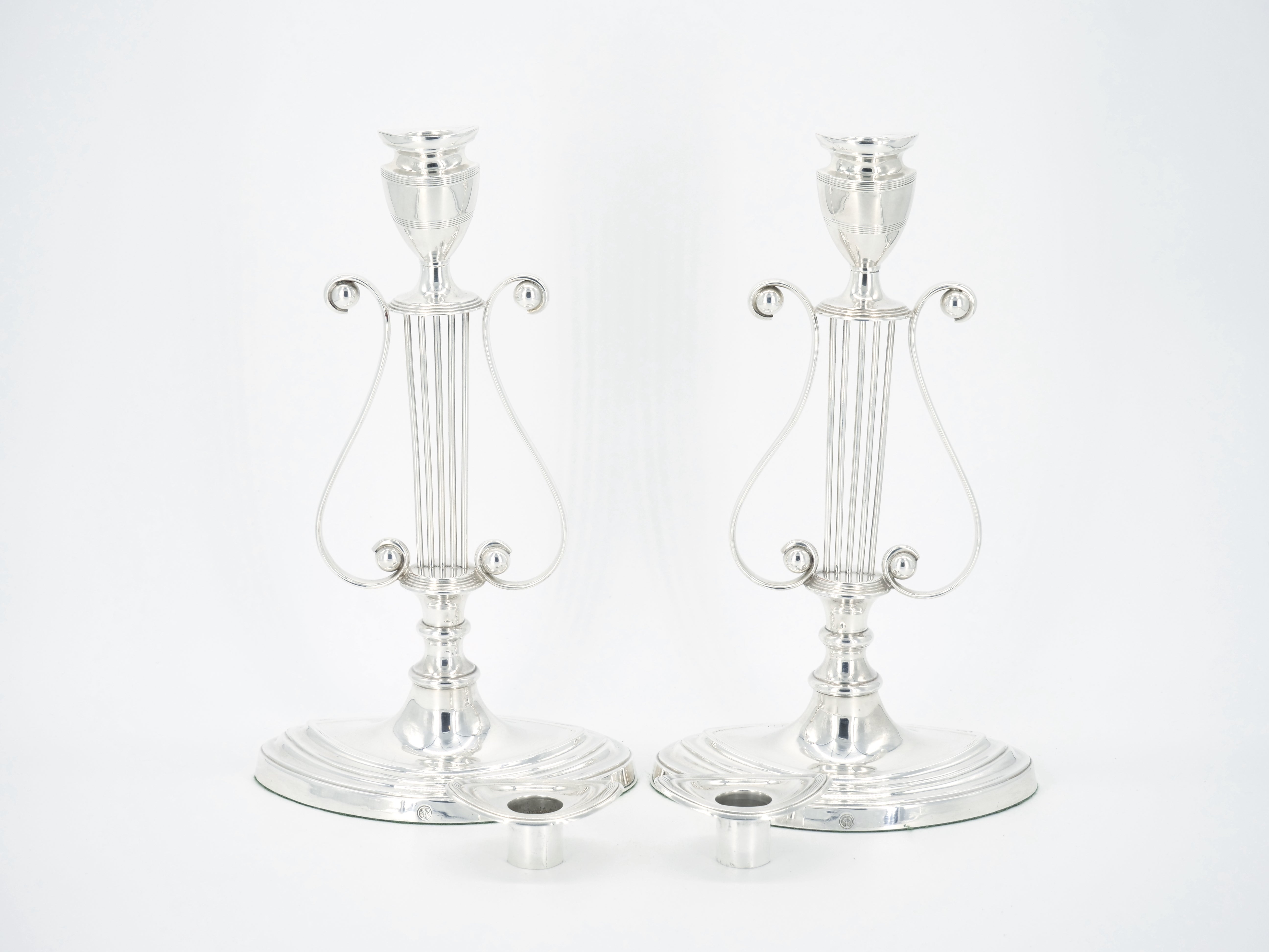 
English silver plate pair tableware candle holder with lyre decorated design motif resting on an oval base. Each candle features a removable bobeche and lyre formed by two elegant opposing s-shaped scrolls and five vertical 