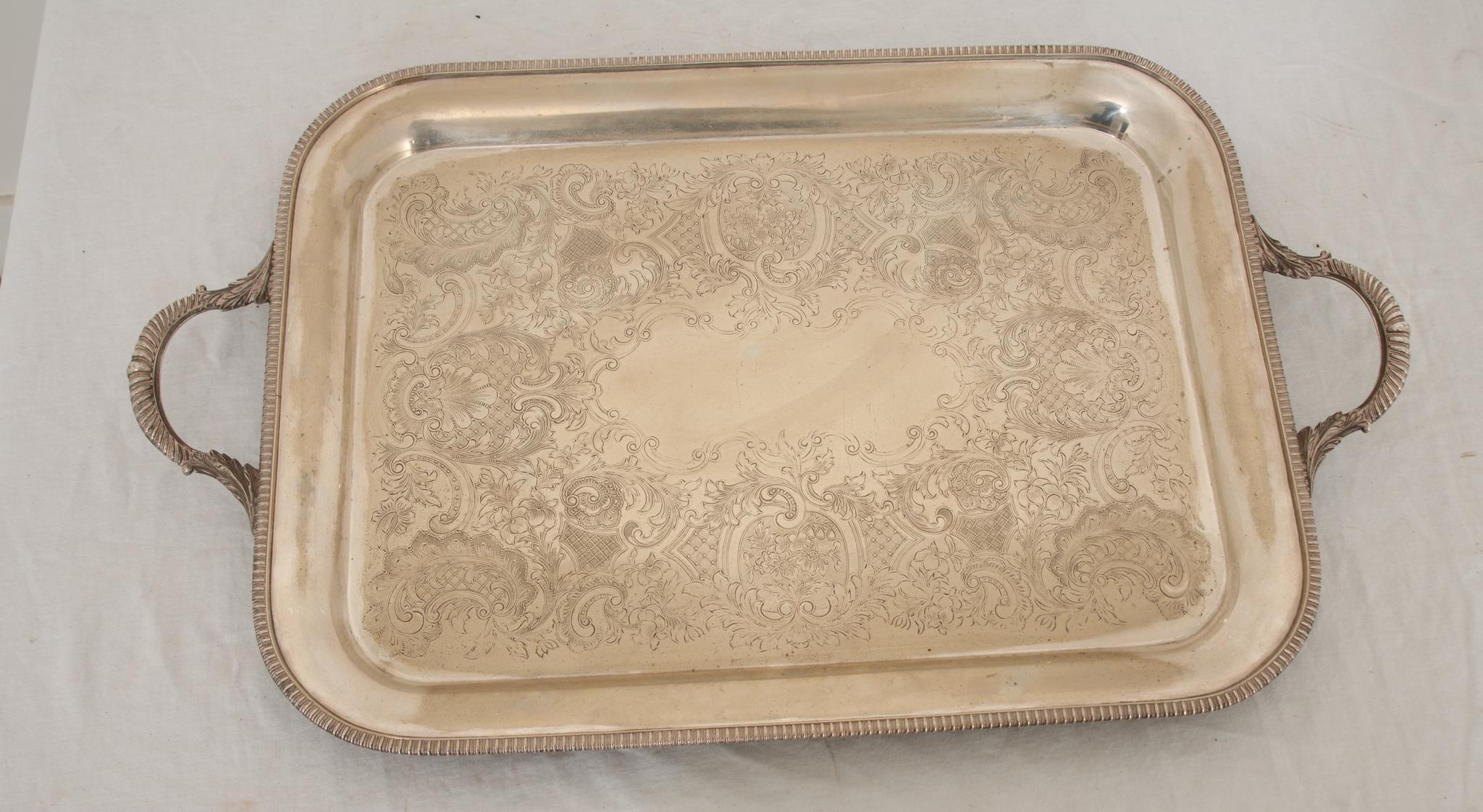A superb English silver plated tray. This rectangular tray features a deep set gadrooned border with elegant handles and is decorated with fanciful symmetrical engravings of floral and filigree designs circling a center cartouche. The quality and