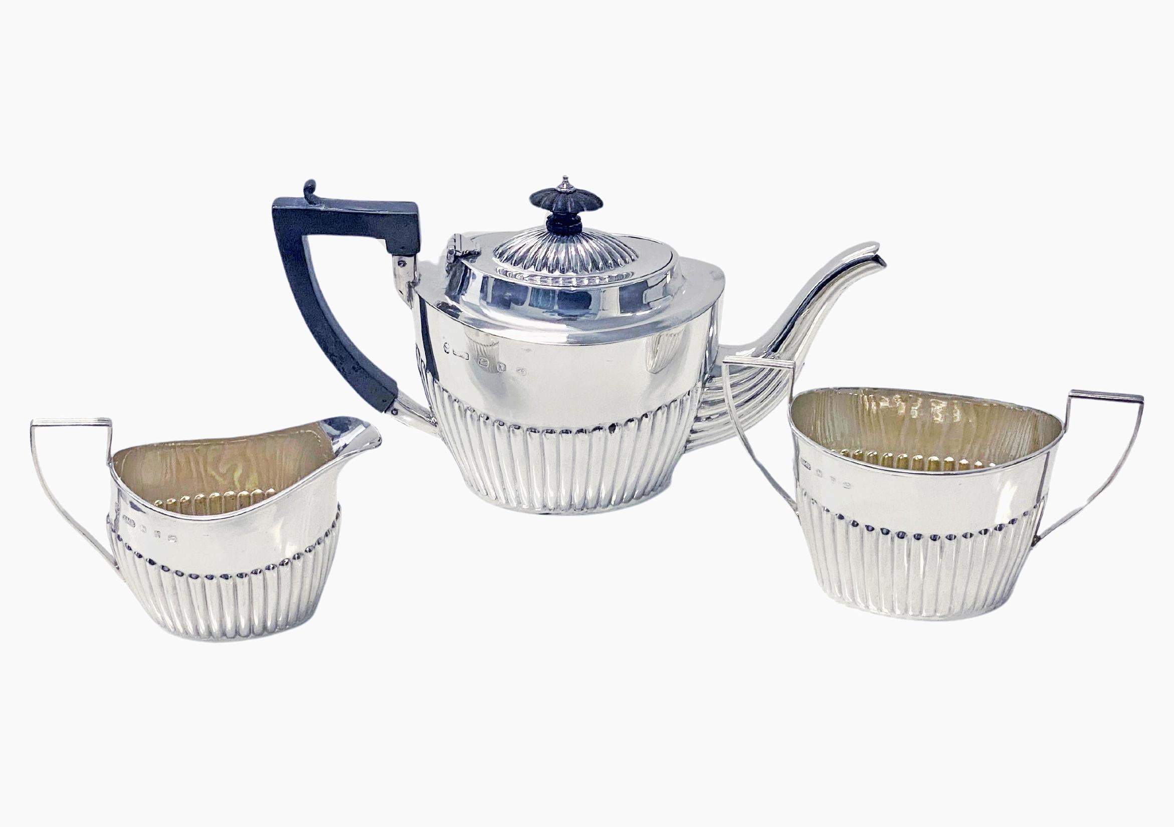 Antique English Silver three-piece Tea Set Birmingham 1896-7 John Millwood Banks retailed by Thornhill London. Comprising teapot, milk and sugar, oval part fluted, carved ebony wood handle and finial to teapot, lightly gilded interiors. Teapot: 8.50