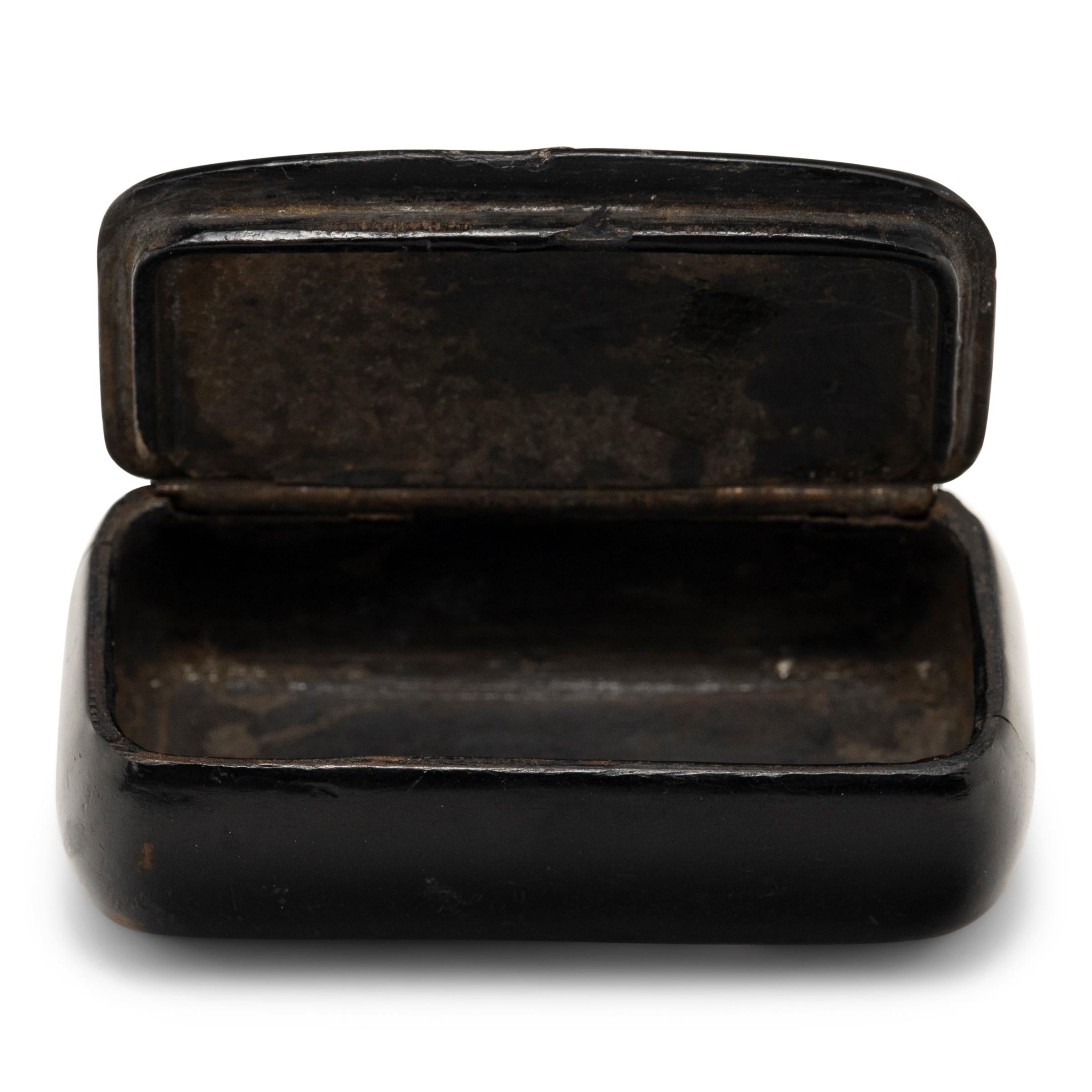 Diese englische Schnupftabakdose aus Pappmaché mit schillernden Perlmutt-Intarsien stammt aus dem späten 19. Jahrhundert. Schwarzer Lack umhüllt das Pappmaché-Gehäuse und bildet eine robuste, aber verführerische Hartschale. Die unregelmäßigen
