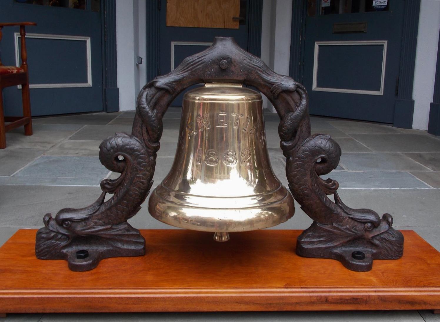 English solid brass ship’s bell from the “S.S. Venetian”. The engraved bell is mounted to the original mythical intertwined dolphin cast iron yoke and is attached to a rectangular carved molded edge Moca wood base for display. Moca wood is