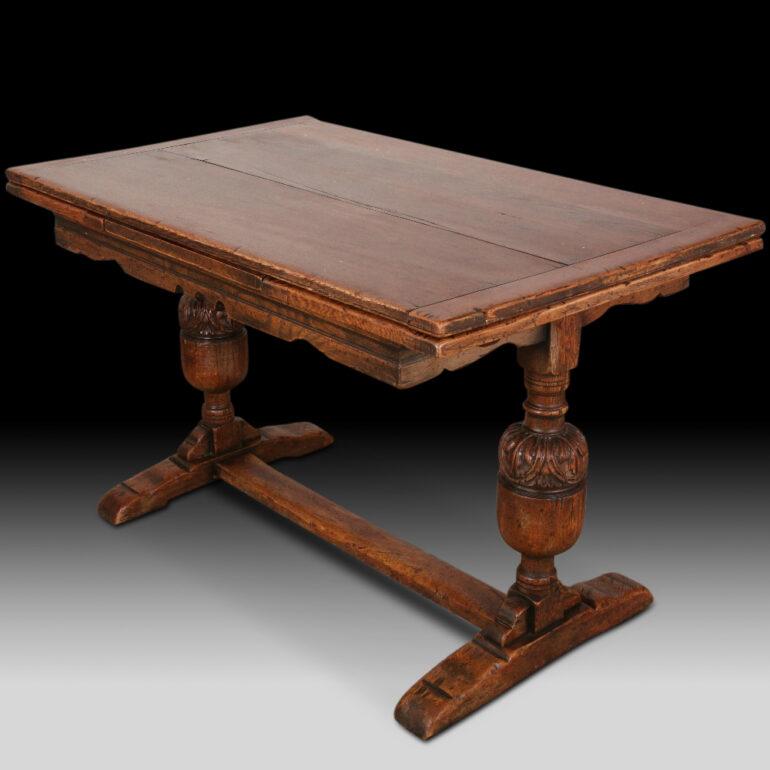 English solid plank oak ‘Jacobean-Revival’ draw leaf trestle or refectory table having a pull-out leaf at each end and raised on a pair of baluster turned and carved legs above wide oak feet and united by a sturdy oak stretch base. A smaller-scale
