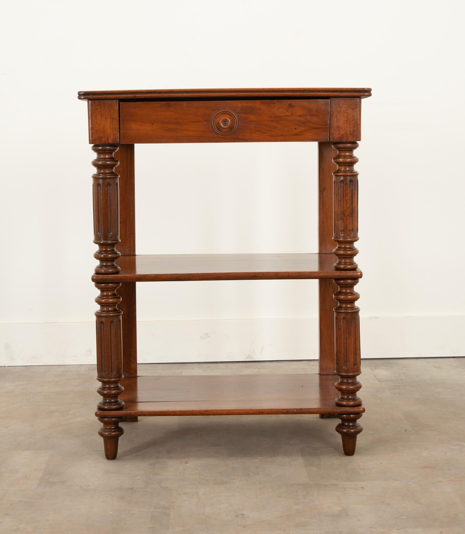 Une étagère en noyer massif simple et raffinée. Le plateau met en valeur le grain de bois distinctif et présente un bord moulé. Un seul tiroir est logé dans le tablier et coulisse facilement à l'aide d'une petite tirette tournée et encerclée. Les