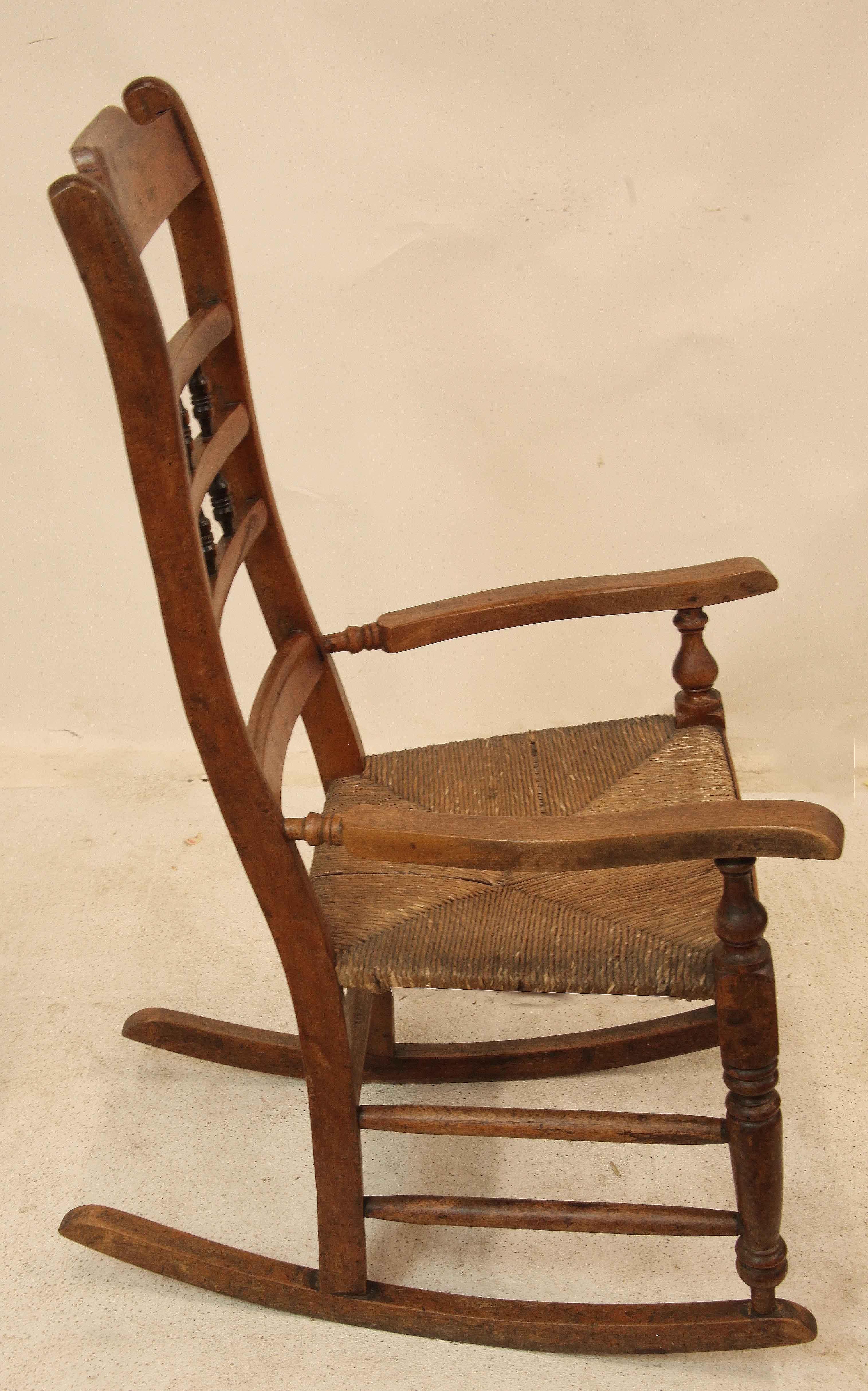 English spindle back rocker, this gently rocking chair is very comfortable, having arms and a tall serpentine shaped back.  There are two rows of three spindles in the splat,  rush seat; the front legs are turned with double turned stretchers ,