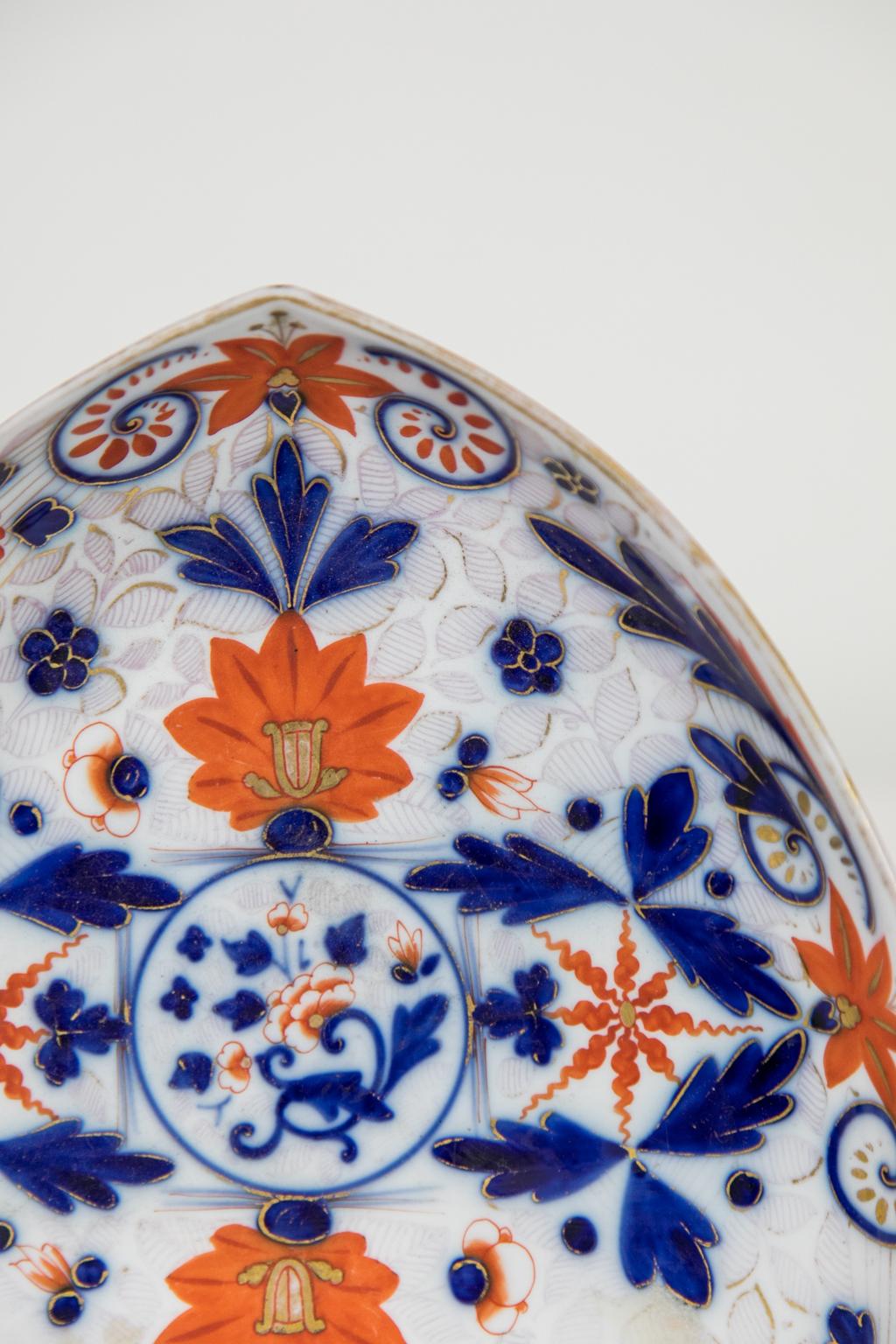This serving dish has a shield shape with red and blue floral and leaf designs. While there is no identifying mark the decoration, glaze, and shape of the underfoot would indicate a date of manufacture circa mid-19th century. The gilding has