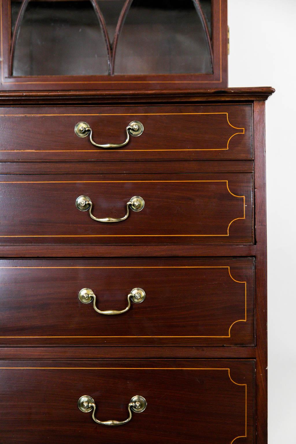 The top of this English inlaid mahogany bookcase has simulated inlaid dentil molding. The top and lower section have inlaid boxwood stringing with the original hardware. The waist molding is later. There are three adjustable shelves in the upper