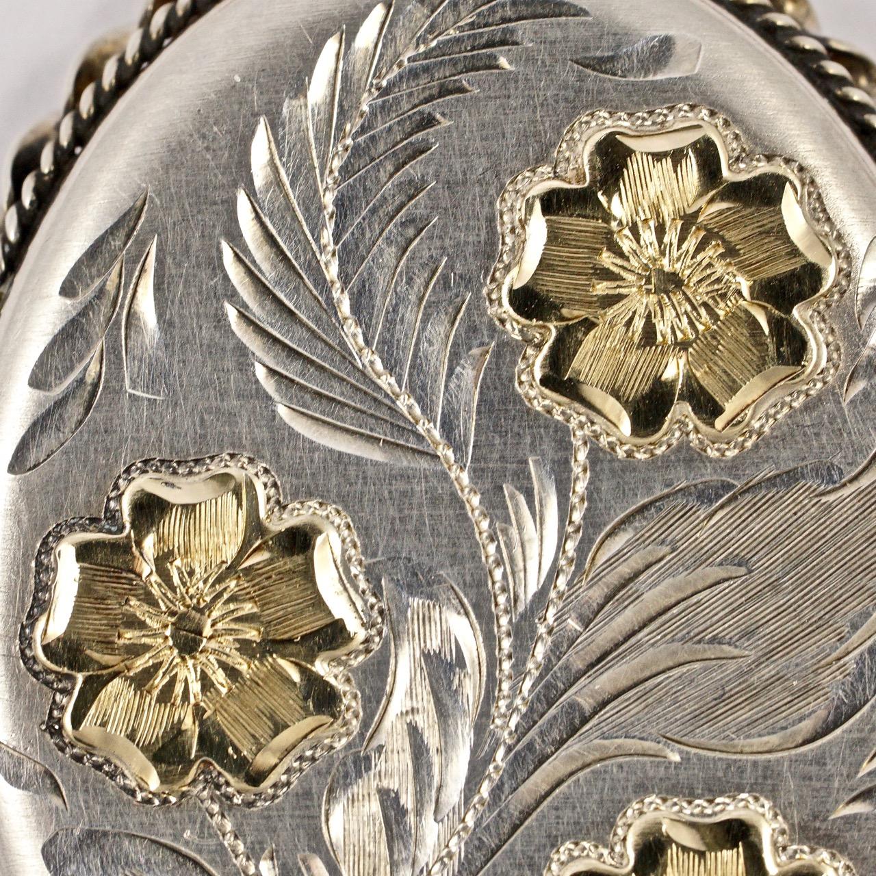 
Sterling silver large locket and chain, featuring a lovely engraved floral design with gold gilded flowers to the front, and an engraved leaves design to the back. The locket is stamped with a lion, an anchor, and the date letter is 'M'. The makers