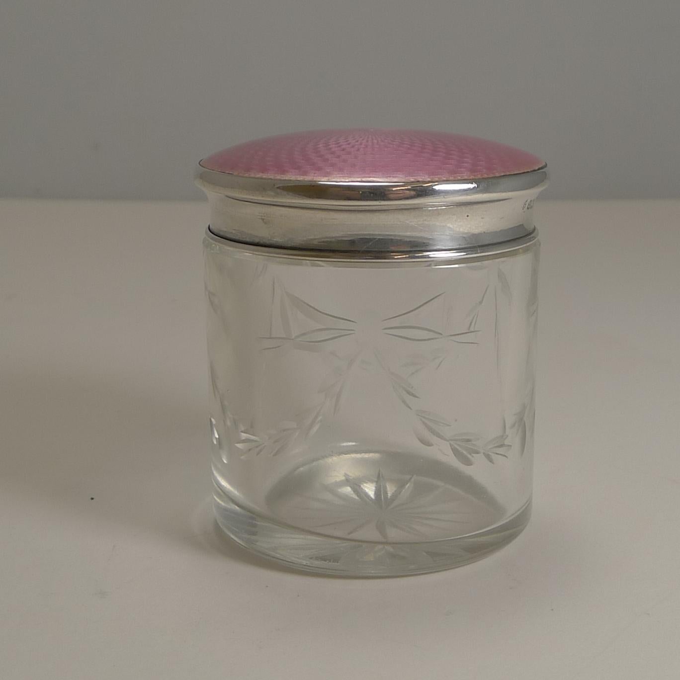 A stunning heavy crystal vanity jar or box with a pretty ribbon and bow garland hand-engraved around the outside.

The sterling silver lid is topped with the most sought-after color of guilloche enamel, a pretty pink with a good bright patina