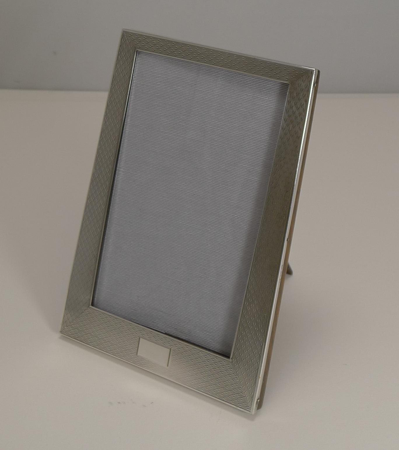 A very smart vintage sterling silver photograph frame in a true Art Deco style, shaped, wider at the bottom and tapering to the top.

The silver is beautifully engine-turned with a vacant rectangular cartouche to the bottom. The back incorporates