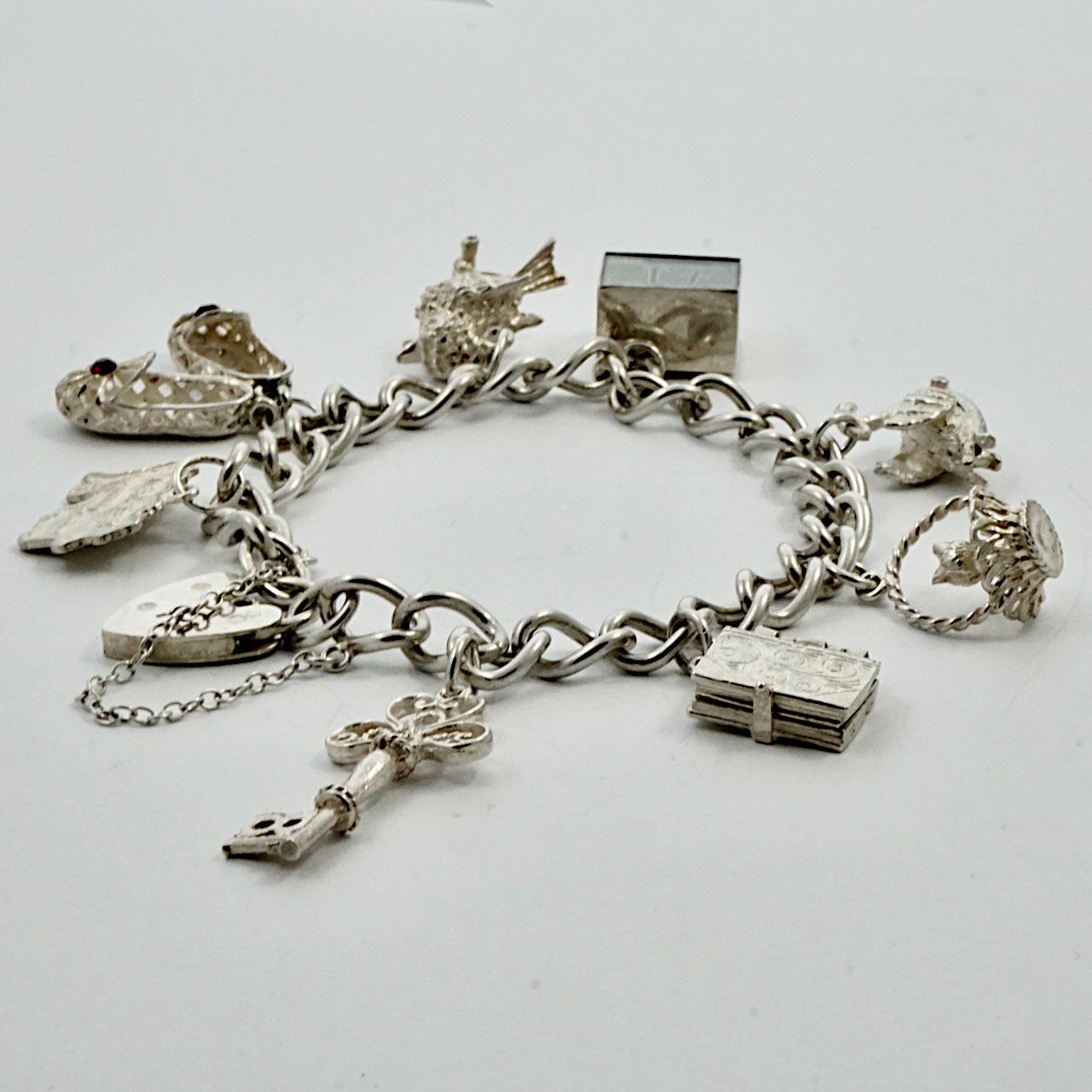 Delightful English sterling silver charm bracelet with a heart lock and chain. There are eight charms: 18 key, opening bible with verses inside, cat in a basket, opening swan with a ballerina inside, encased emergency £1 note, bird, red jewelled