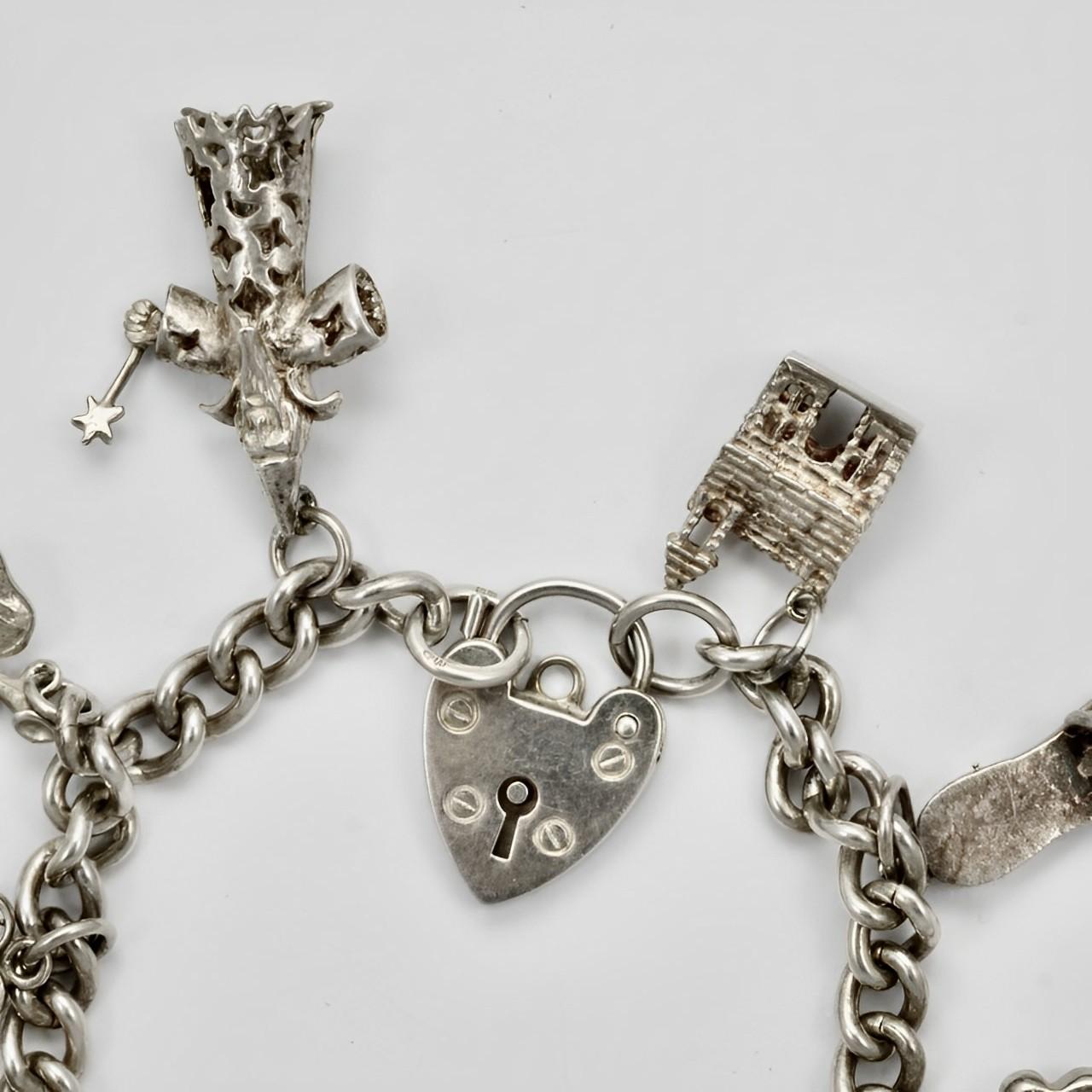 Delightful English sterling silver charm bracelet with a heart lock clasp. The safety chain is missing. There are ten charms: 2 x 21 keys, wizard, four leaf clover, opening house with a person inside, Noah's ark, trolley with a moving wheel, Chinese