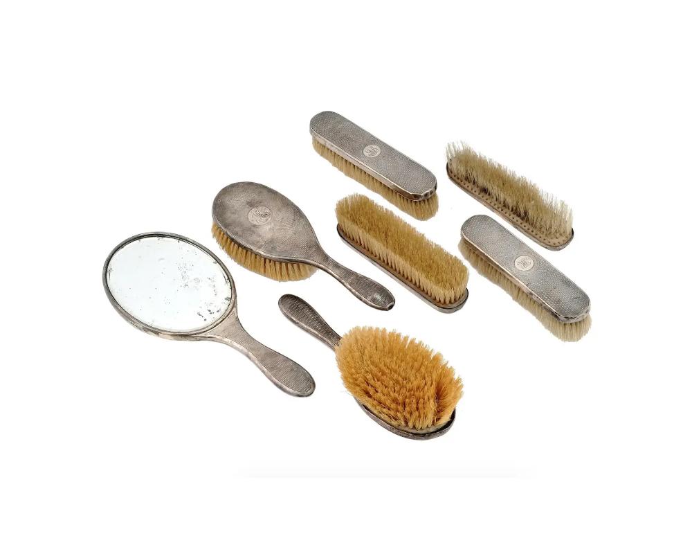 A lot of antique early 20th-century English sterling silver brushes. A total of 7 items including a mirror, two handled hair brushes, and four clothes brushes. The guilloche backside of each piece is decorated with engraved initials MB. London assay