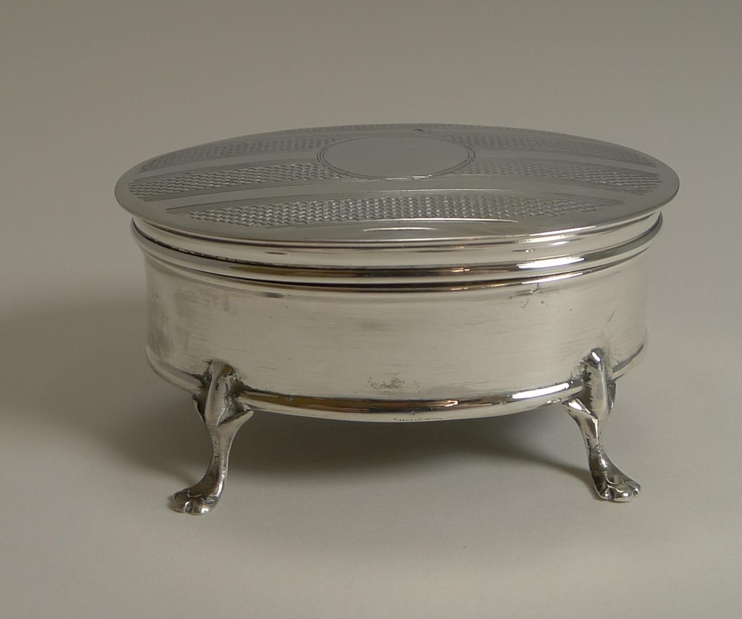 A smart little jewelry / ring box standing on four legs.

The hinged lid is decorated with an engine turned striped design with a central circular vacant cartouche. Once the lid is opened the gilded underside is revealed. The box retains its