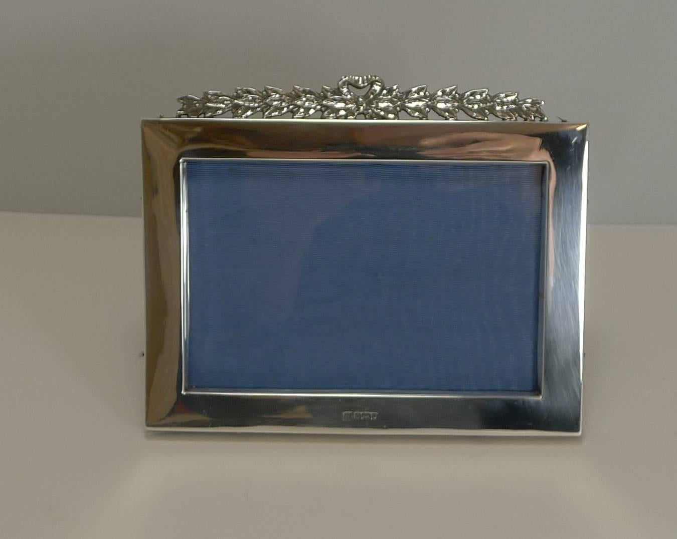 A stunning English Edwardian photograph frame made from sterling silver, with a popular and harder to find landscape configuration.

The top is beautifully crowned with an elongated ribbon and bow mount.

The silver is fully hallmarked for the