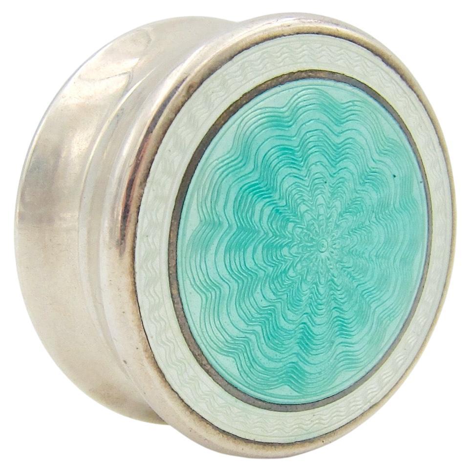 An antique Edwardian sterling silver pill box — perfectly sized for small items of jewelry. The removable lid is decorated with a field of translucent icy blue enamel framed by a band of white over delicate, engine-turned patterning. The small round