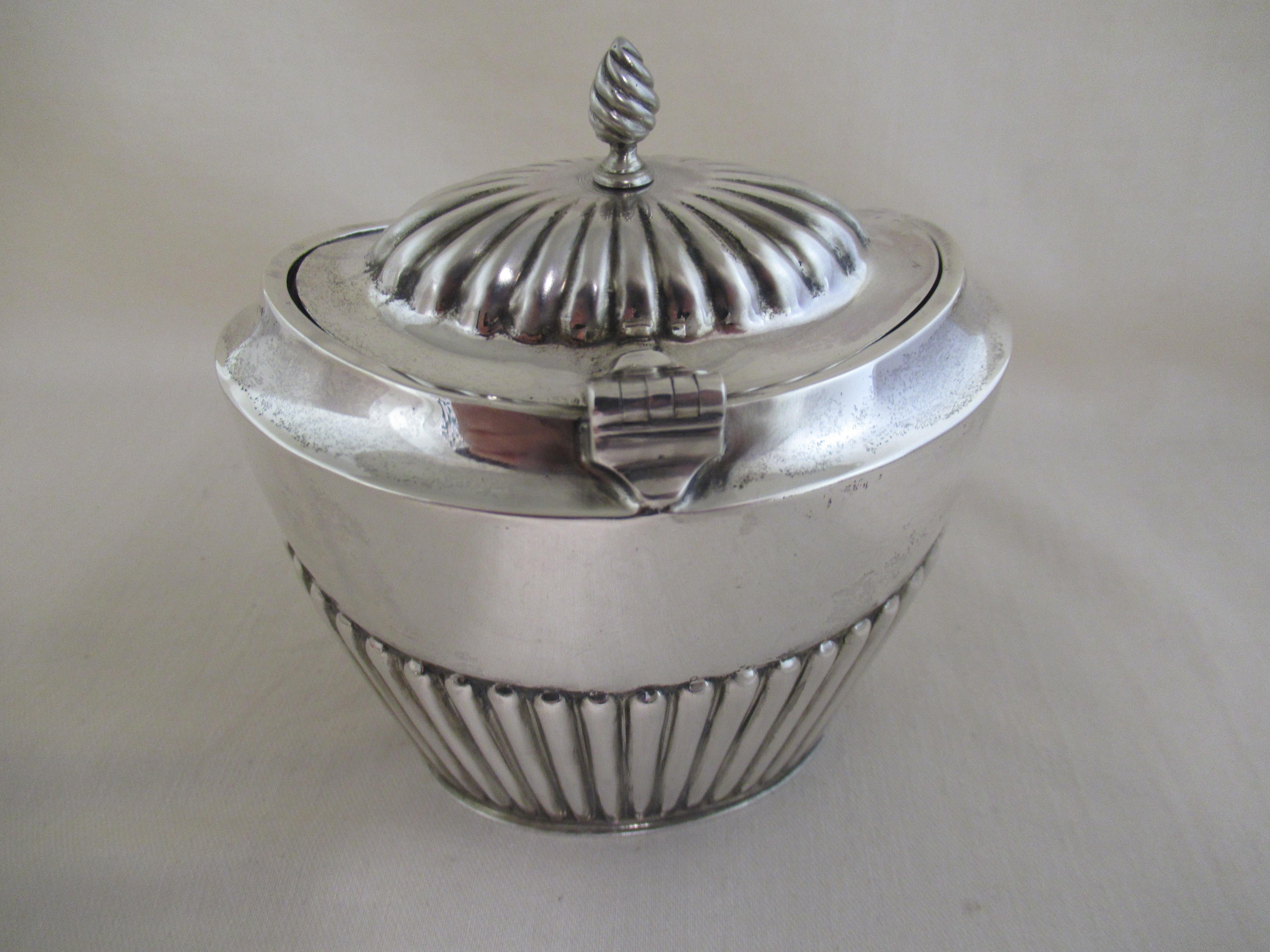 Sterling Silver - Oval Tea Caddy 
Made in 1909, ( 114 years old), by Barker Brothers, Constitution Hill. Birmingham.
 
A full set of hallmarks applied by the Chester Assay Office:- 
 Sword + Sheaves of Corn - Chester Assay Office mark.
 Lion -