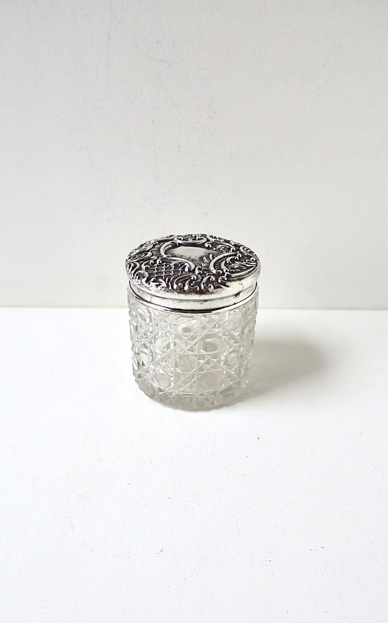 An English sterling silver and cut-glass vanity, dresser, or bath/powder room jar box, Victorian period, circa late-19th century, England. The sterling silver top/lid has a repose floral design around with a center area that can be monogramed is so