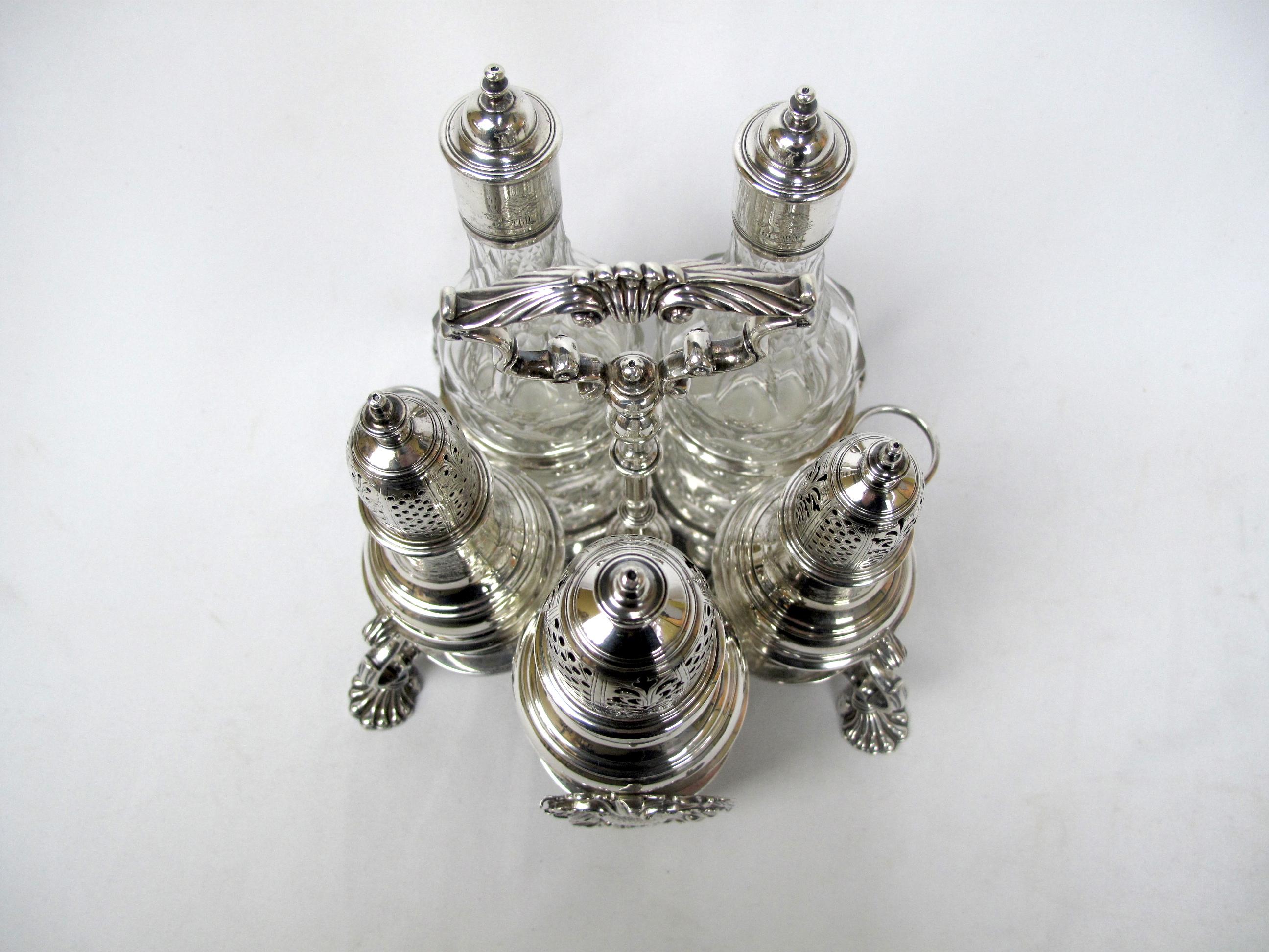 English sterling silver “Warwick” type cruet set. It features a matching set of 3 baluster shaped silver castors with pull of tops and 2 silver and faceted glass oil and vinegar bottles and a four footed sterling silver stand with handle.. The