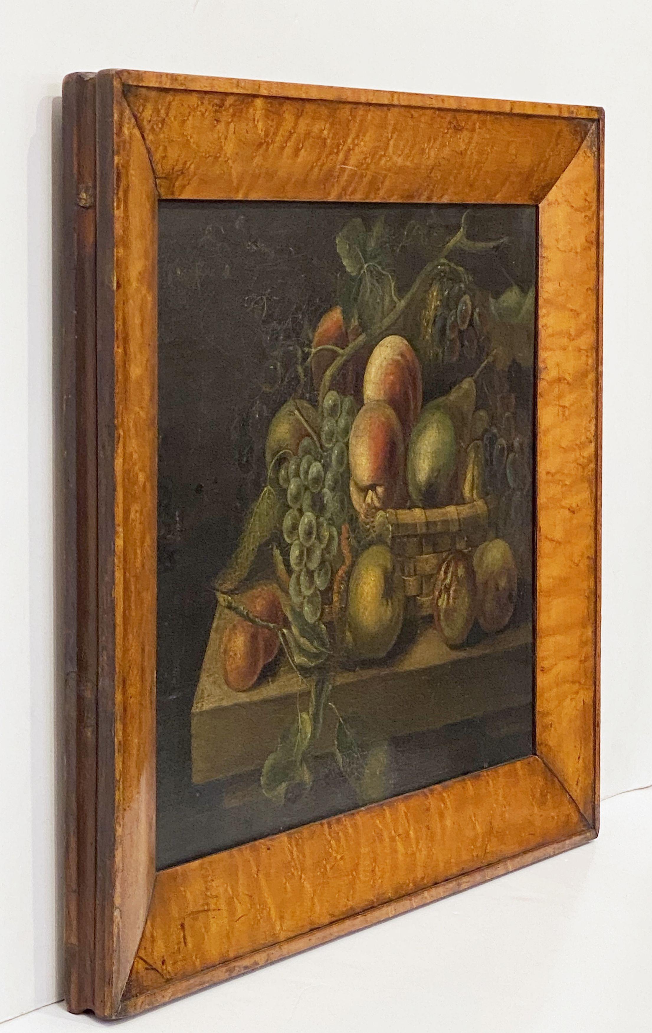 A fine English oil painting from the 19th c. in a beautifully patinated maple frame, featuring a still life of apples, pears, peaches and grapes arranged in a wicker basket. The painting is on canvas, and then mounted to board.