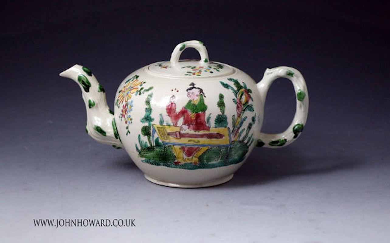 Dated: 1760 Staffordshire England UK

The stoneware teapot with original cover is a globular shape and decorated in enamel colors and a saltglaze. 
The chinoiserie type decoration is profusely and expertly applied to show a female musician and a