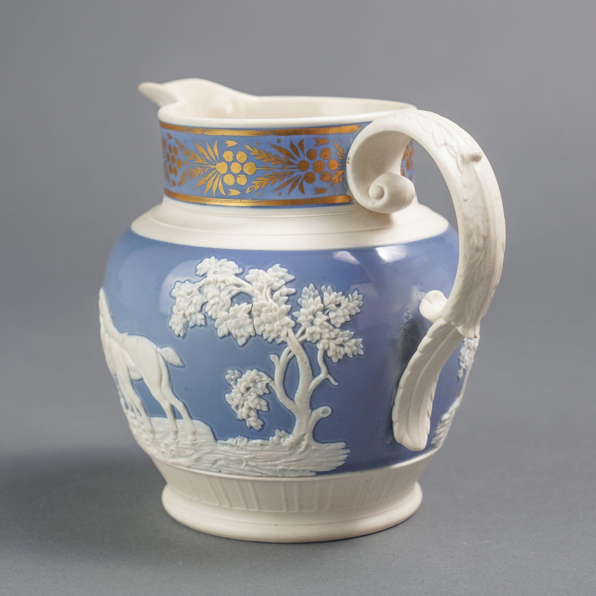 Feldspathic stoneware hunt jug with applied handle. The hunt scene relief rests on a ground of blue enamel. The neck of the pitcher has a gilt trailing decoration in the Classical taste, also on a blue enamel ground. Attributed to Chetham &