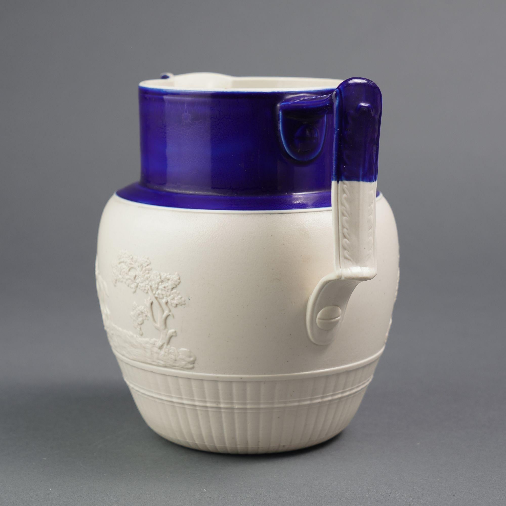Feldspathic stoneware hunt jug with a cobalt blue enameled neck and spout. The body of the pitcher is decorated with an applied hunt scene above a melon ribbed base.

Written in graphite on the underfoot: At Cumberland Forge when Grandmother comes