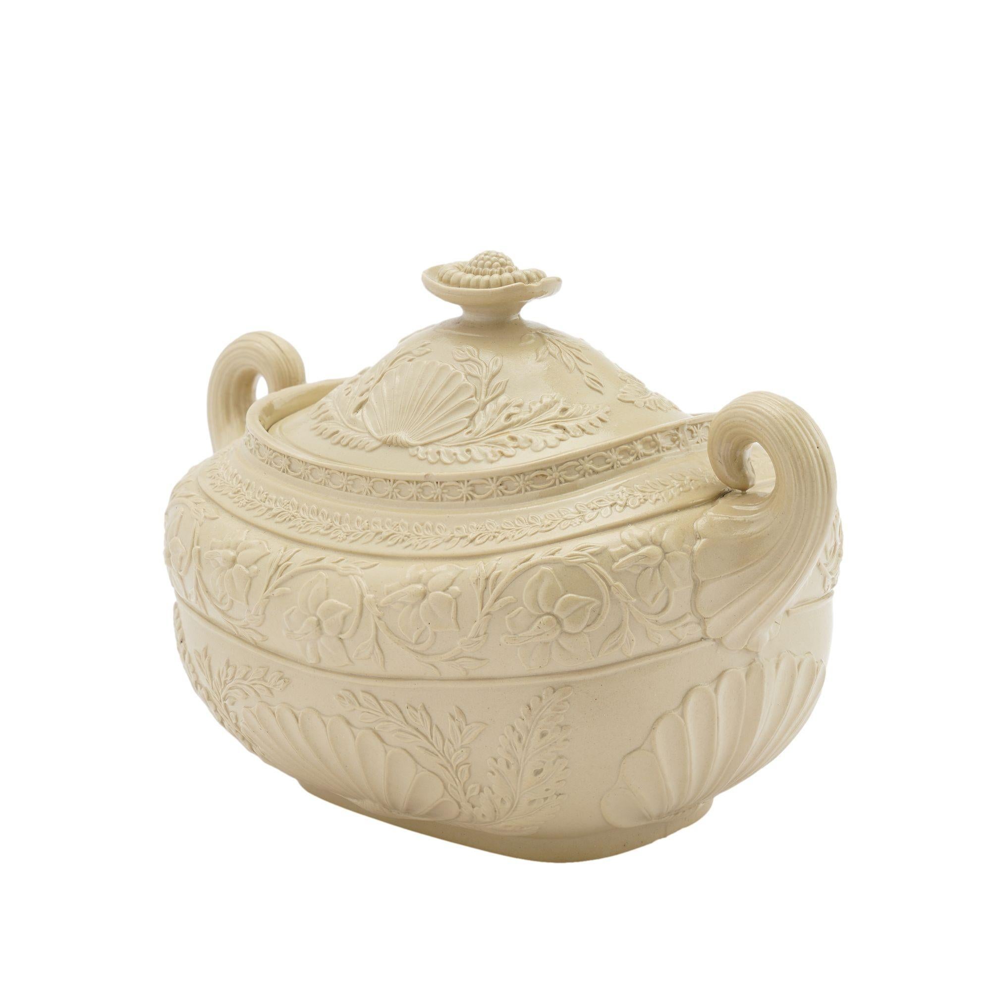 A stoneware sugar bowl in a putty color with fine smear glaze. The double pistol grip handles flank the impressed floral and shell motif covering the surface of the bowl and cover. Unmarked.

Staffordshire, England, circa 1830.