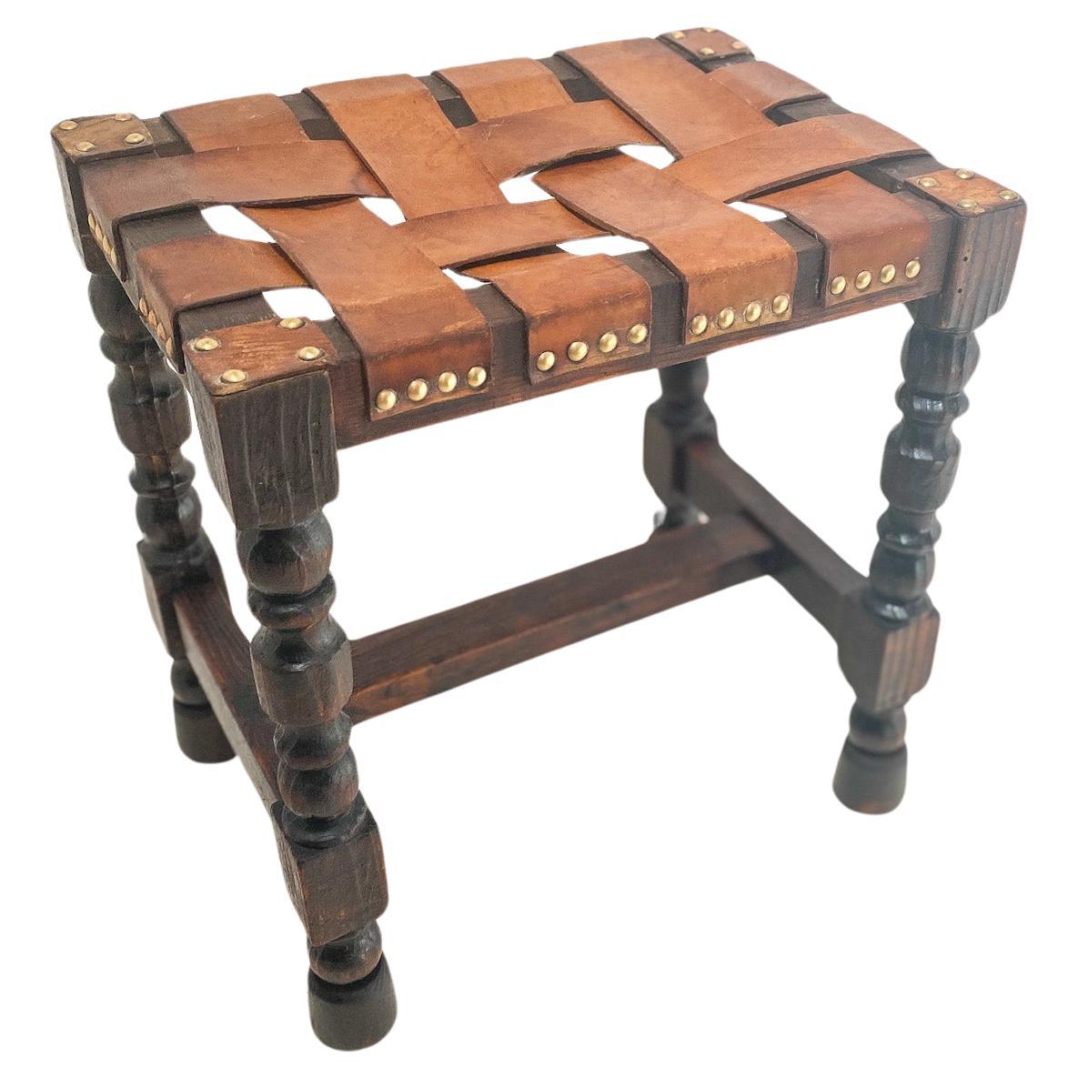 20th Century oak stool from England, the top is in a cross of Leather Straps . Legs are in a twisted carved shape. This is in a brown color.