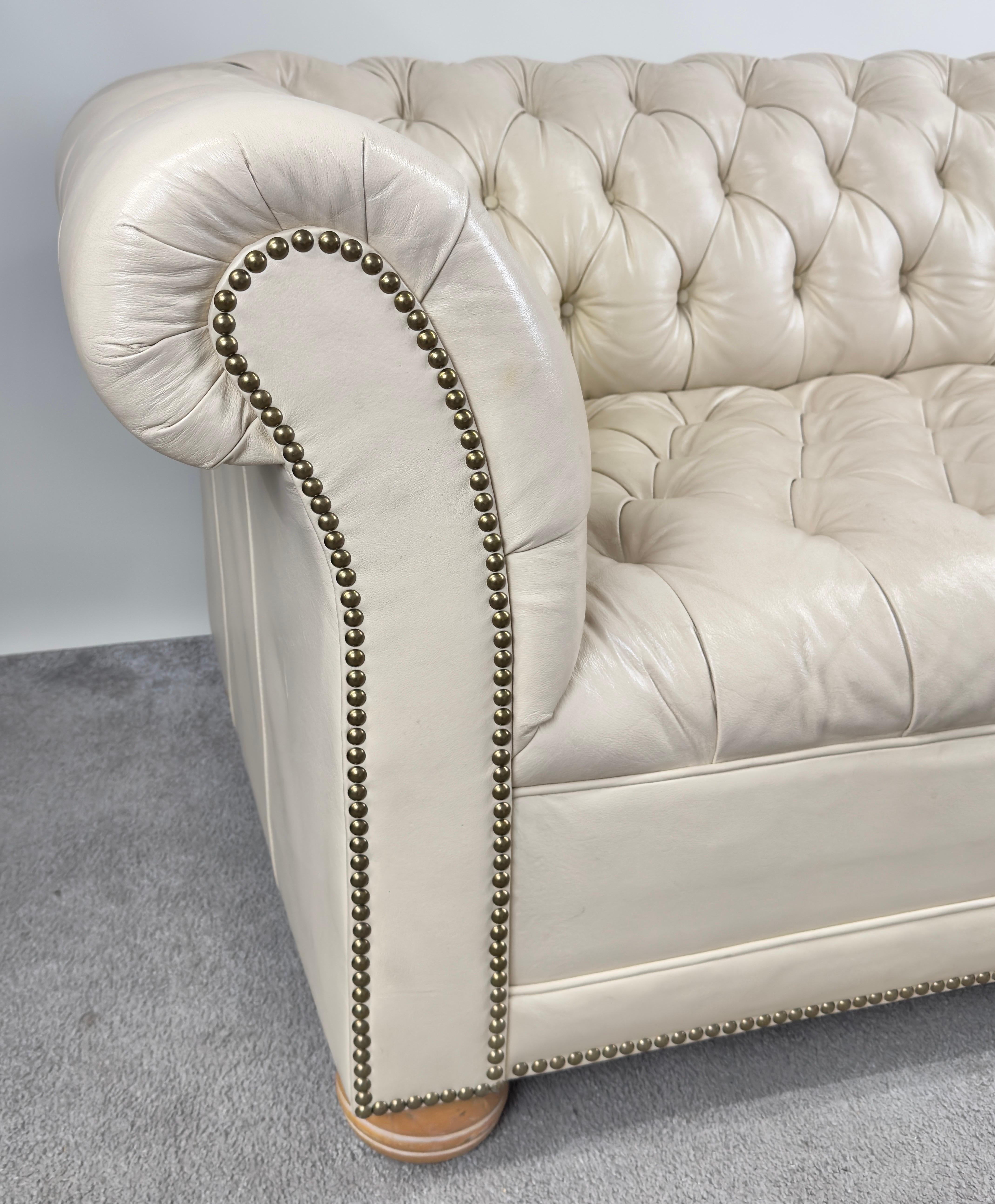 Uno squisito divano Chesterfield rivestito in una lussuosa pelle bianco sporco che emana raffinatezza. La caratteristica trapuntatura a bottoni, meticolosamente realizzata a mano, abbellisce sia lo schienale che le aree di seduta, creando un effetto