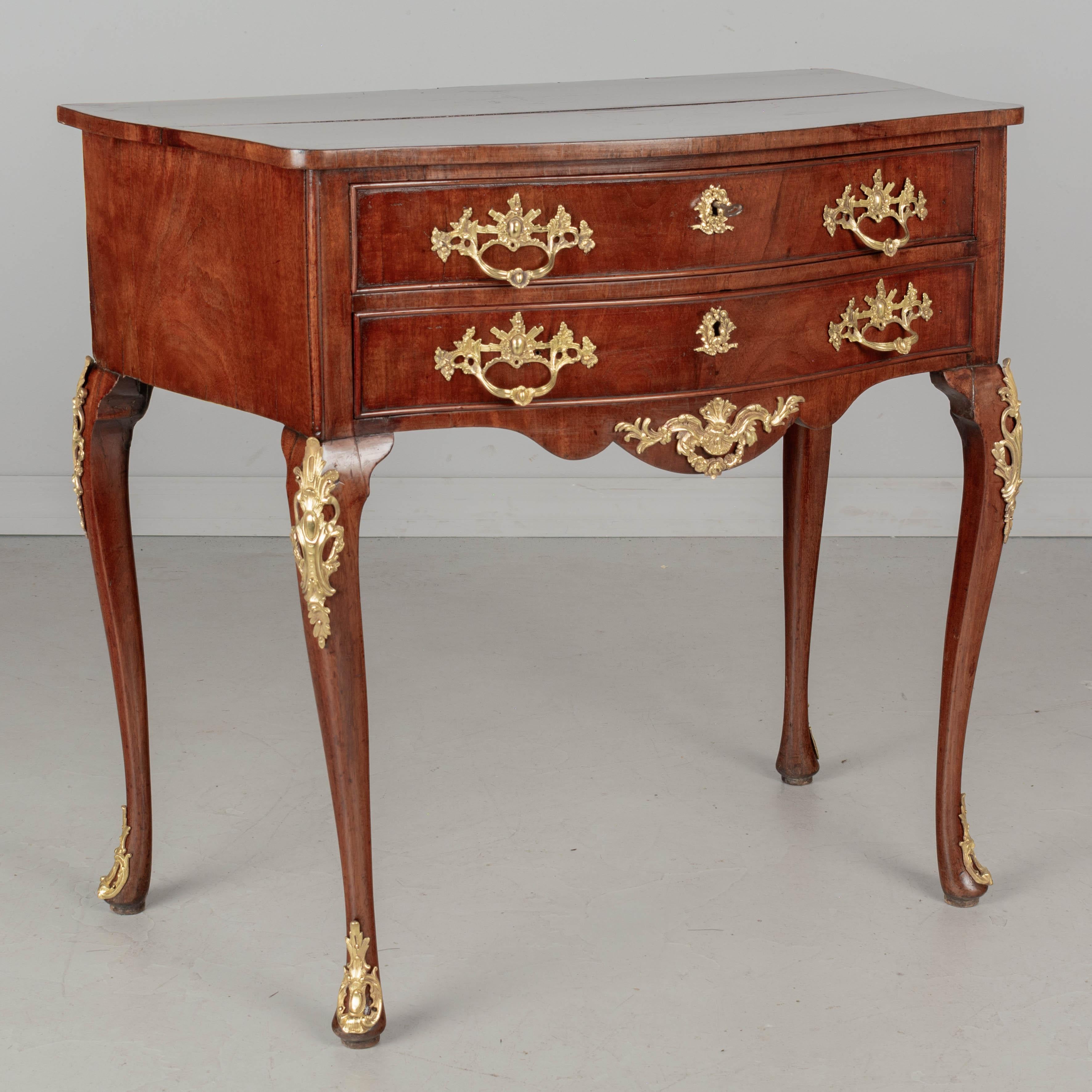 An English style mahogany serpentine chest made of solid and veneers of mahogany. Two dovetailed drawers with original polished cast bronze hardware, working locks and one key. Oak as a secondary wood. Good condition with restoration on one leg.