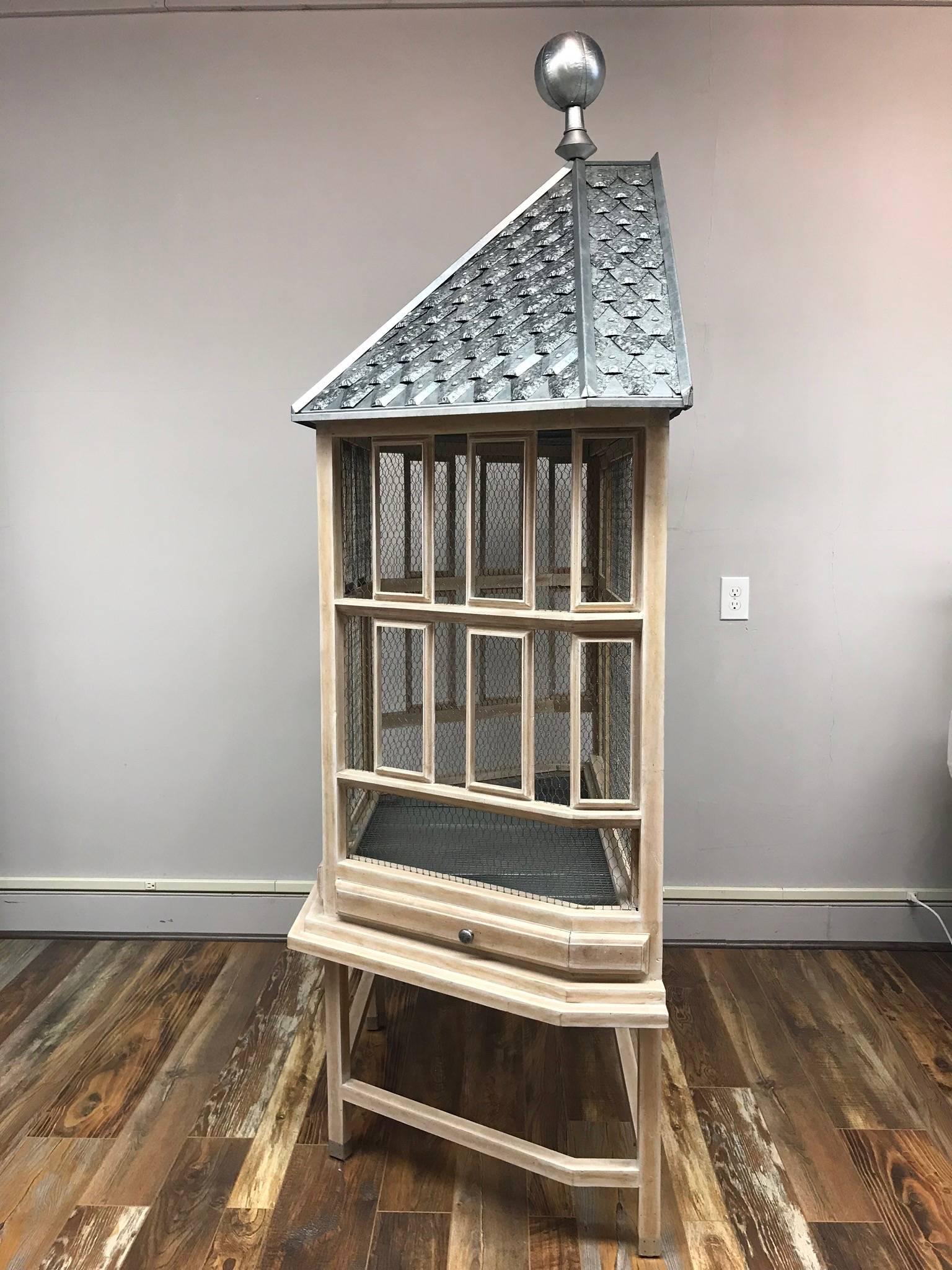 A wood-and-metal bird cage topped with a charming metal tile “roof” and finial that would be perfect for filling with ferns and other plants. Open the chicken wire doors and embrace a world of fun. A true statement piece for any room. White-washed
