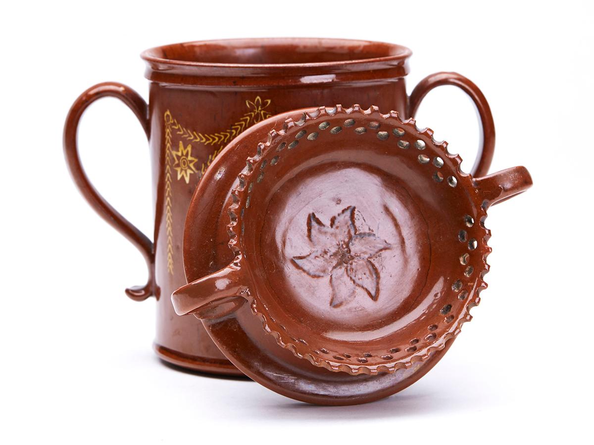 A rare antique English Sussex slipware redware pottery twin handled cup with a twin handled cover with decorative raised and pierced rim and decorated with an incised floral design dated 1819. The cup is of cylindrical shape, finely potted with