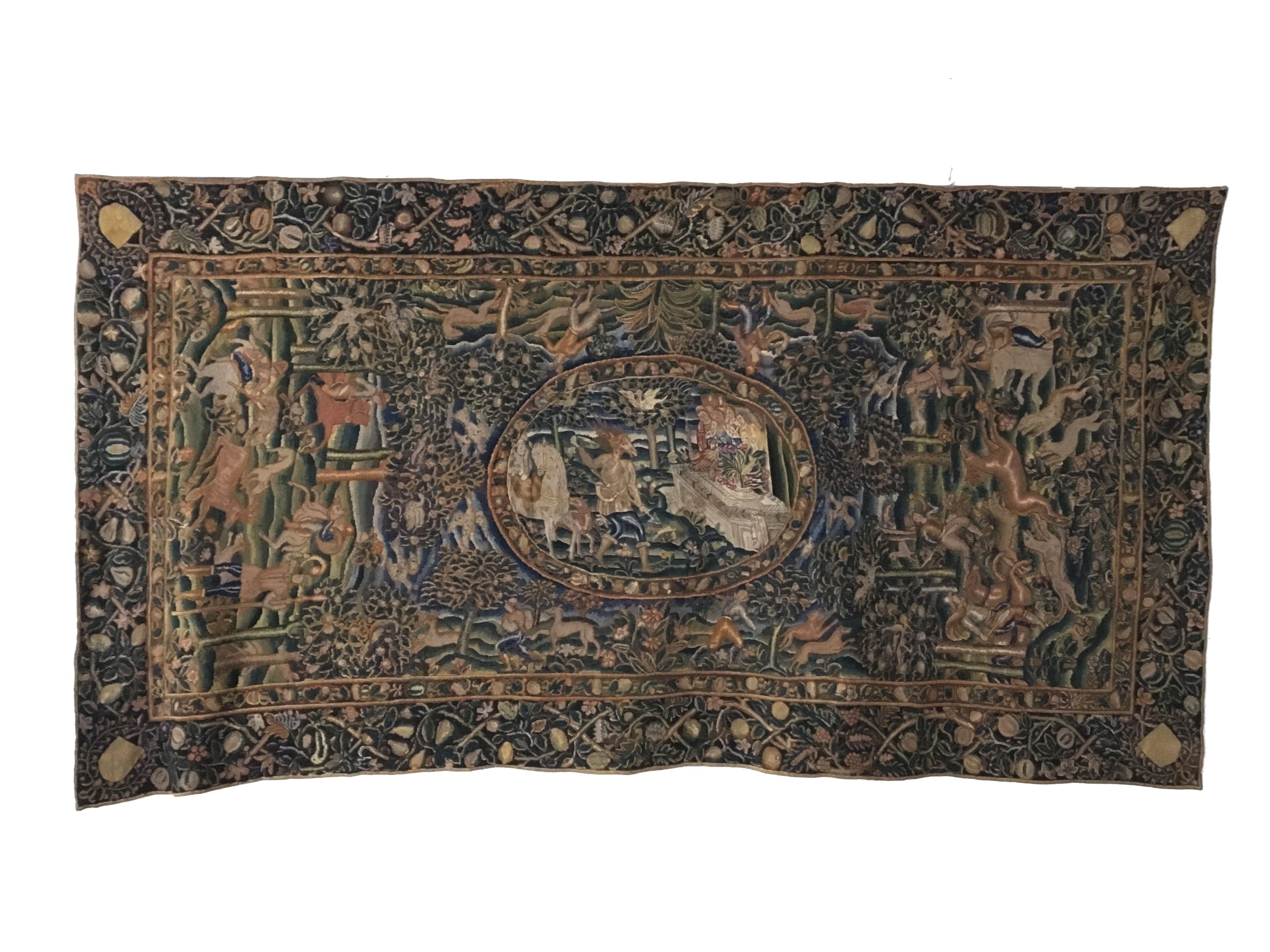 A fine and very rare 17th century table tapestry worked in richly colored silks and wools. The oval allegorical centre panel depicting Artemis & Acteon, on a field of woodland with huntsmen and dogs in pursuit of stags either side and birds flying