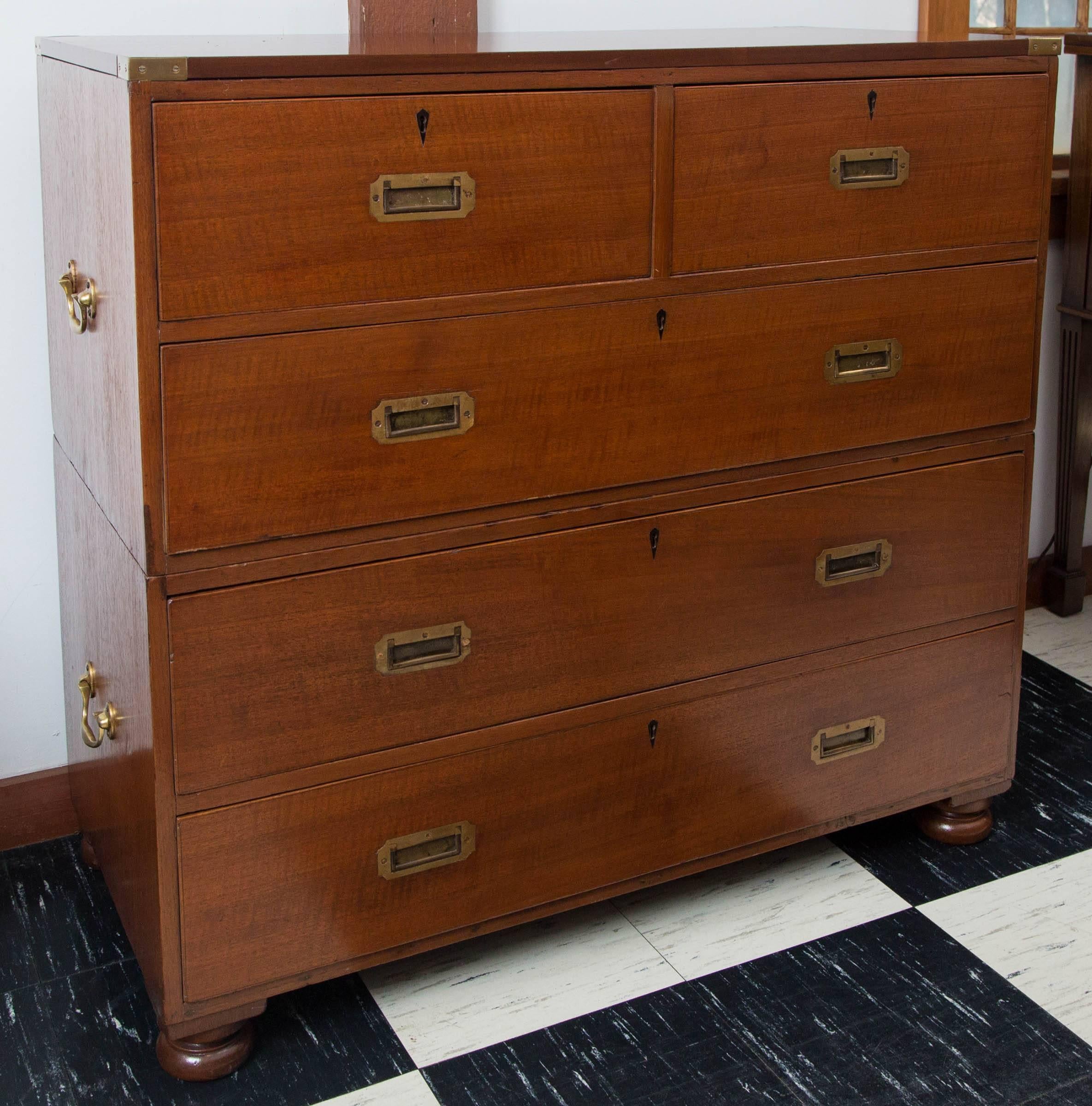 Two-piece English teak campaign chest of drawers with brass handles on upper and lower sections. Chest rests on replaced bun feet.