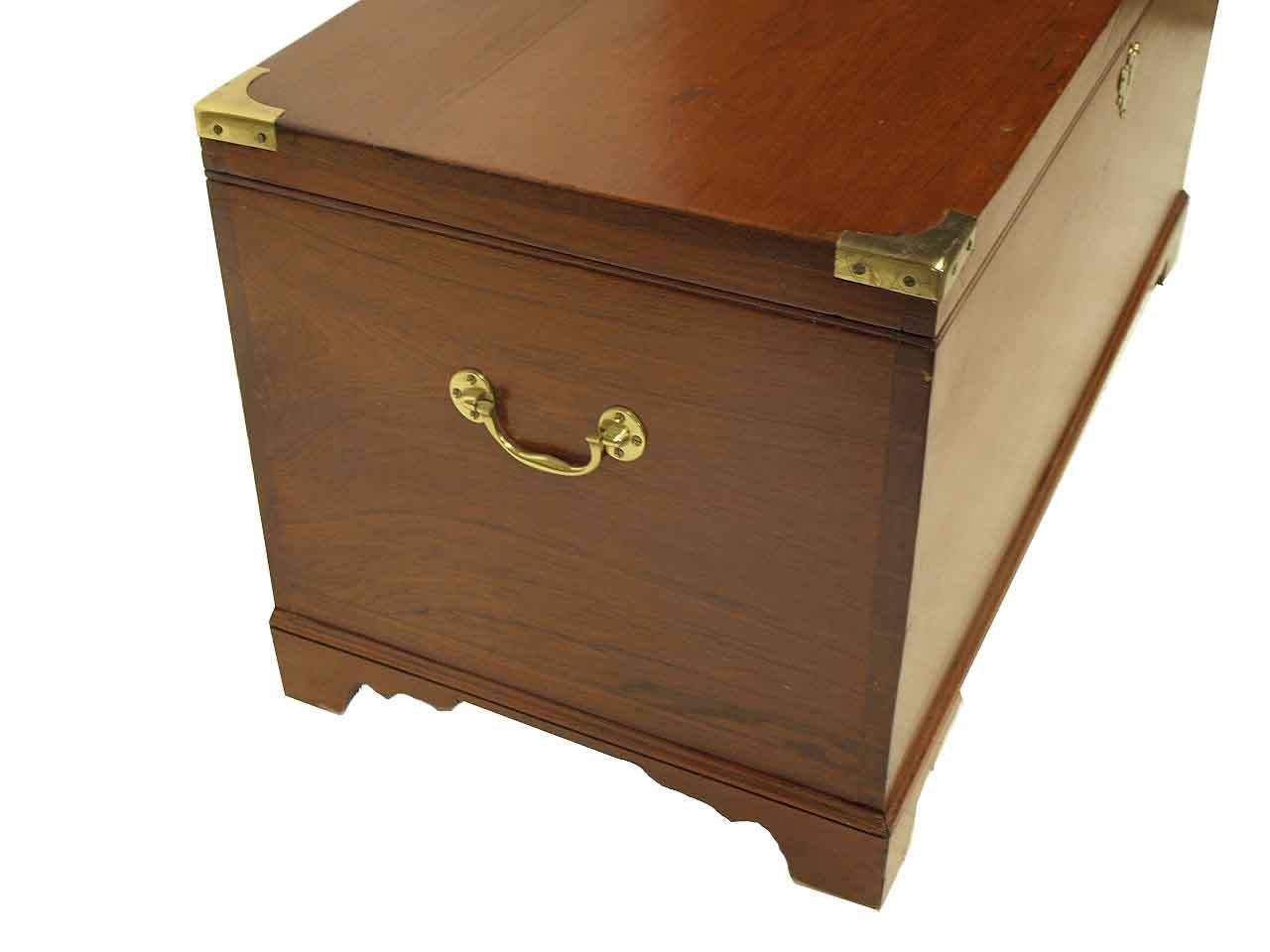 English teak wood blanket chest, the top with brass bound corners, sides with brass carrying handles; open interior, resting on bracket feet. This chest is an excellent size to serve as a coffee table.