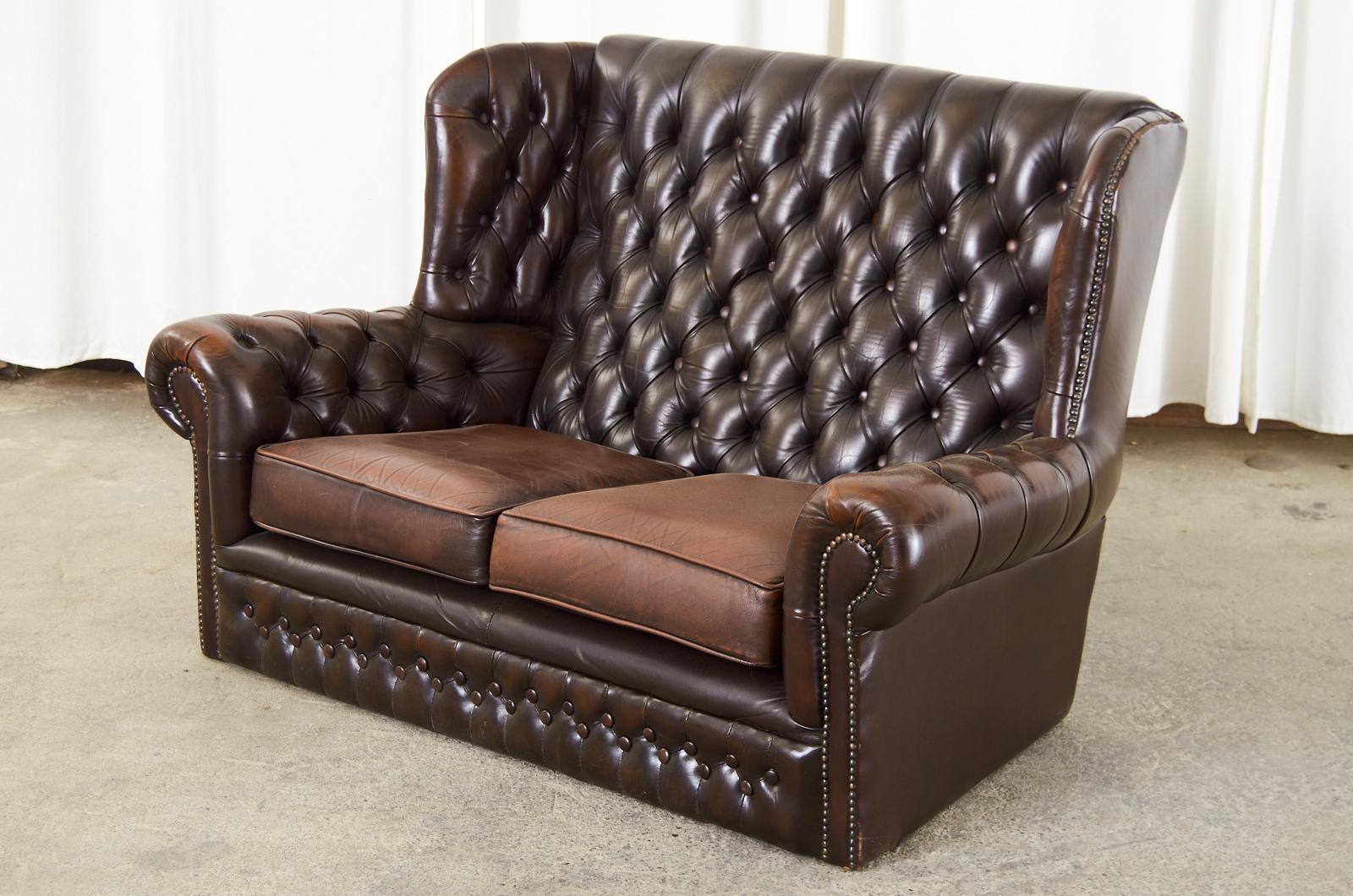 Gorgeous English wingback chesterfield settee sofa featuring a cigar leather tufted upholstery hand-crafted in England by Thomas Lloyd from a hard frame covered with fine Italian full top grain leather hides. Beautifully aged and worn with a soft