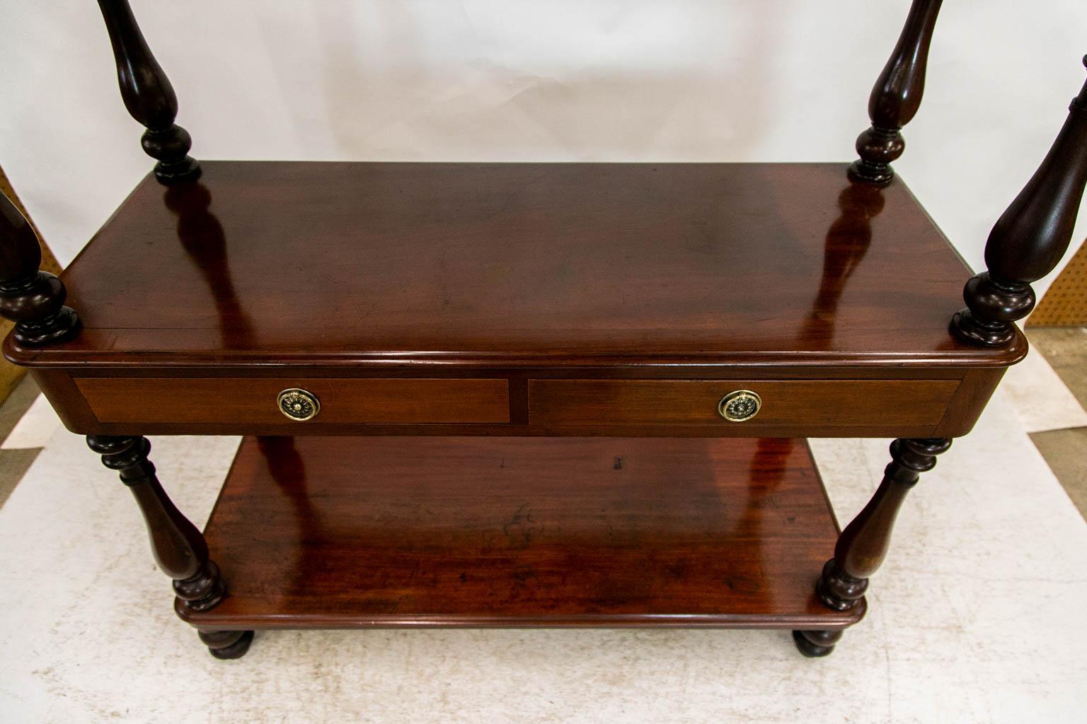 All three shelves of this mahogany server have an ogee shaped molding on four sides. The shelves are supported by four turned columns on each level with turned finials on the top. It is finished on all sides and can be used in the center of a room.