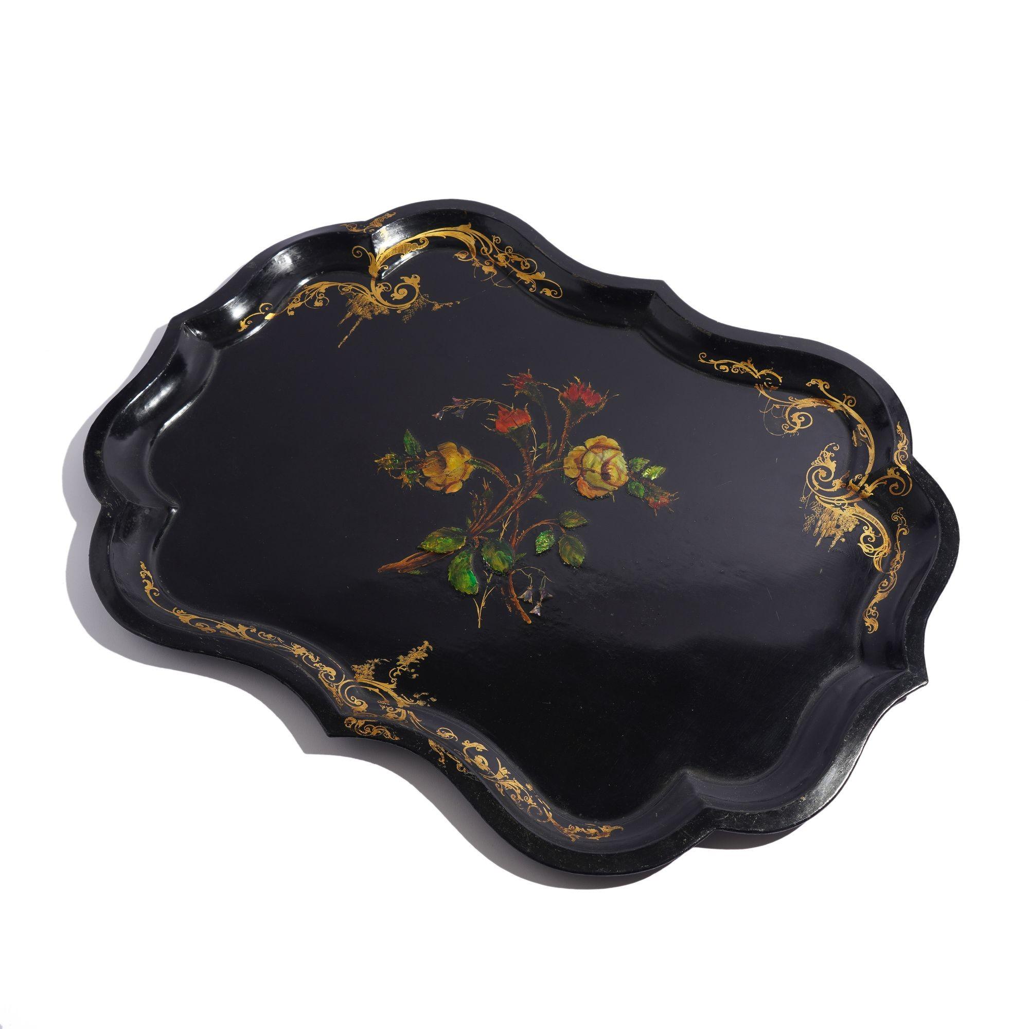 Teetablett aus Zinn in Chippendale-Form mit schwarzem Grund und Perlmutt-Intarsien in der Mitte, die ein Rosenbouquet hervorheben. Die Umrandung ist mit vergoldetem Maßwerk verziert.

England, um 1845.