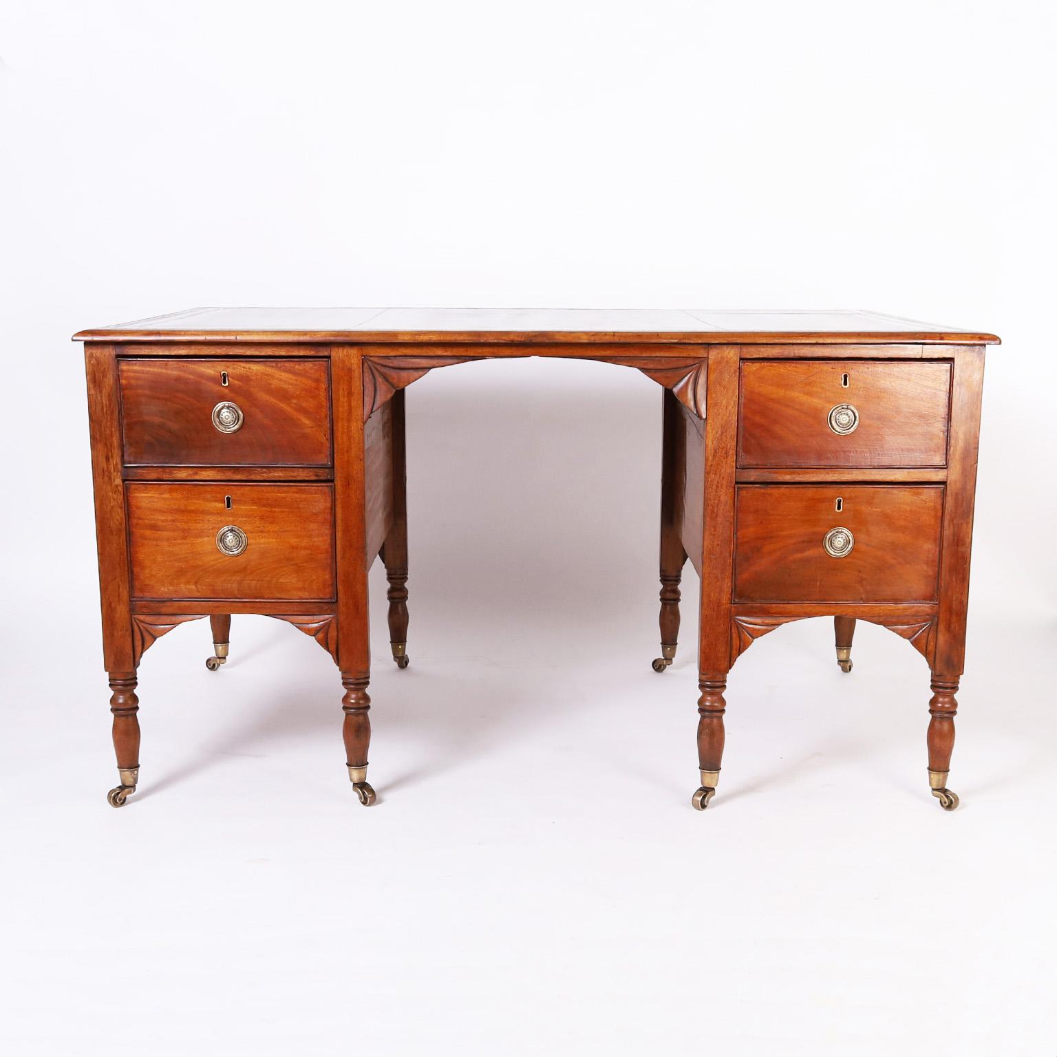 Rare and remarkable antique George III style partners desk with the original tooled green leather top on a mahogany case with four drawers on either side, brass hardware, stylized fan brackets, and turned legs with brass casters.