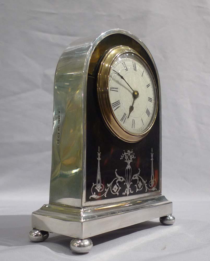 Attractive English silver and tortoiseshell and silver pique mantel clock. The silver case hallmarked for 1921 Birmingham, England. Dome topped silver case on a rectangular base with four silver bun feet. Circular dial within a glass bezel is of