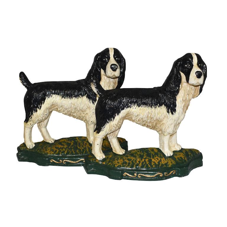 A pair of cast iron door stops or bookends. Created from heavy cast iron, this set of English Springer Spaniels is hand-painted in black, white, green, and gold. Each piece is identical and features a standing dog with black and white fur. The tail