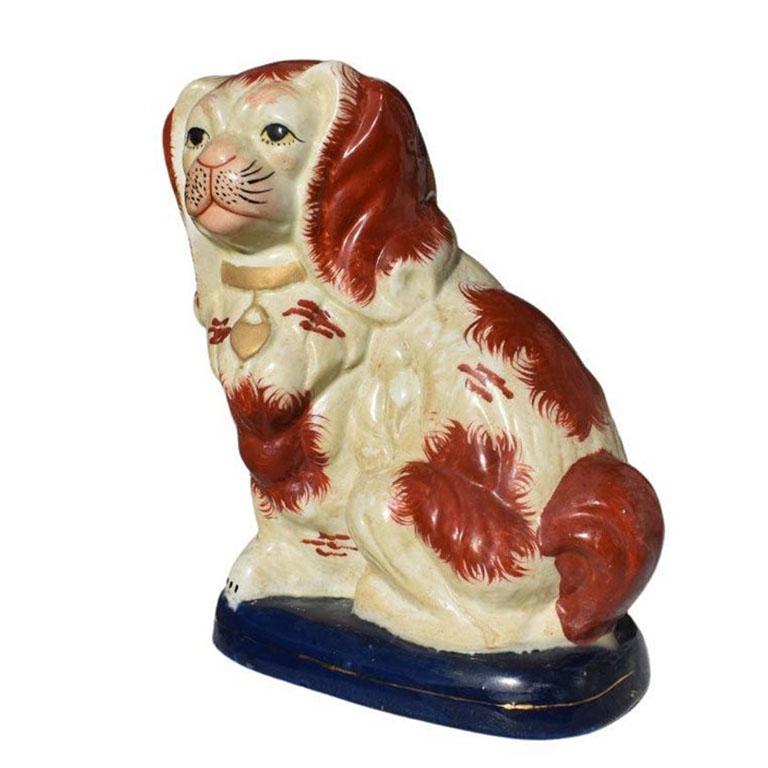 A porcelain King Charles Spaniel ceramic dog in brown, blue, and gold. A timeless piece spotted on the mantles and bookshelves of collectors across the globe. This piece depicts a sweet pup sitting on its hind legs upon a deep blue pillow and sports