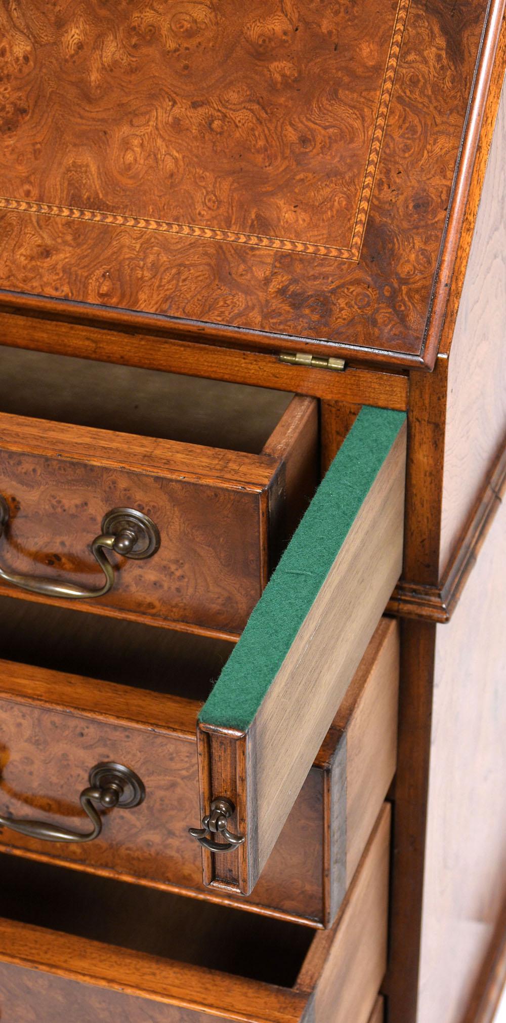 This 1970s English Traditional style slant front desk is covered in bird eye veneers stained a rich walnut color with a lacquered finish. Two arms extend from the front of the desk to support the fold down work area. Inside the desk cabinet there