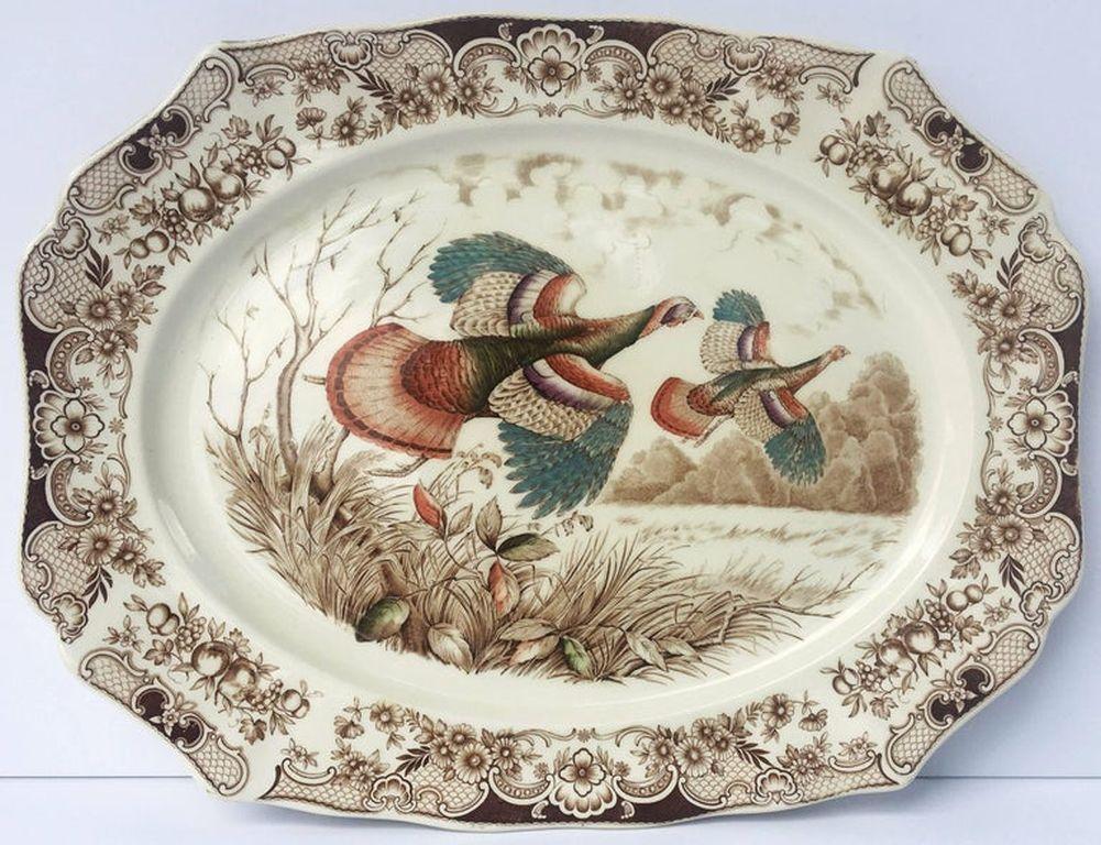 Un grand plat de service vintage présentant le motif des dindes sauvages volant en marron et blanc, réalisé par la célèbre entreprise de poterie anglaise Johnson Brothers.

Avec une étiquette brune authentique du milieu du siècle au