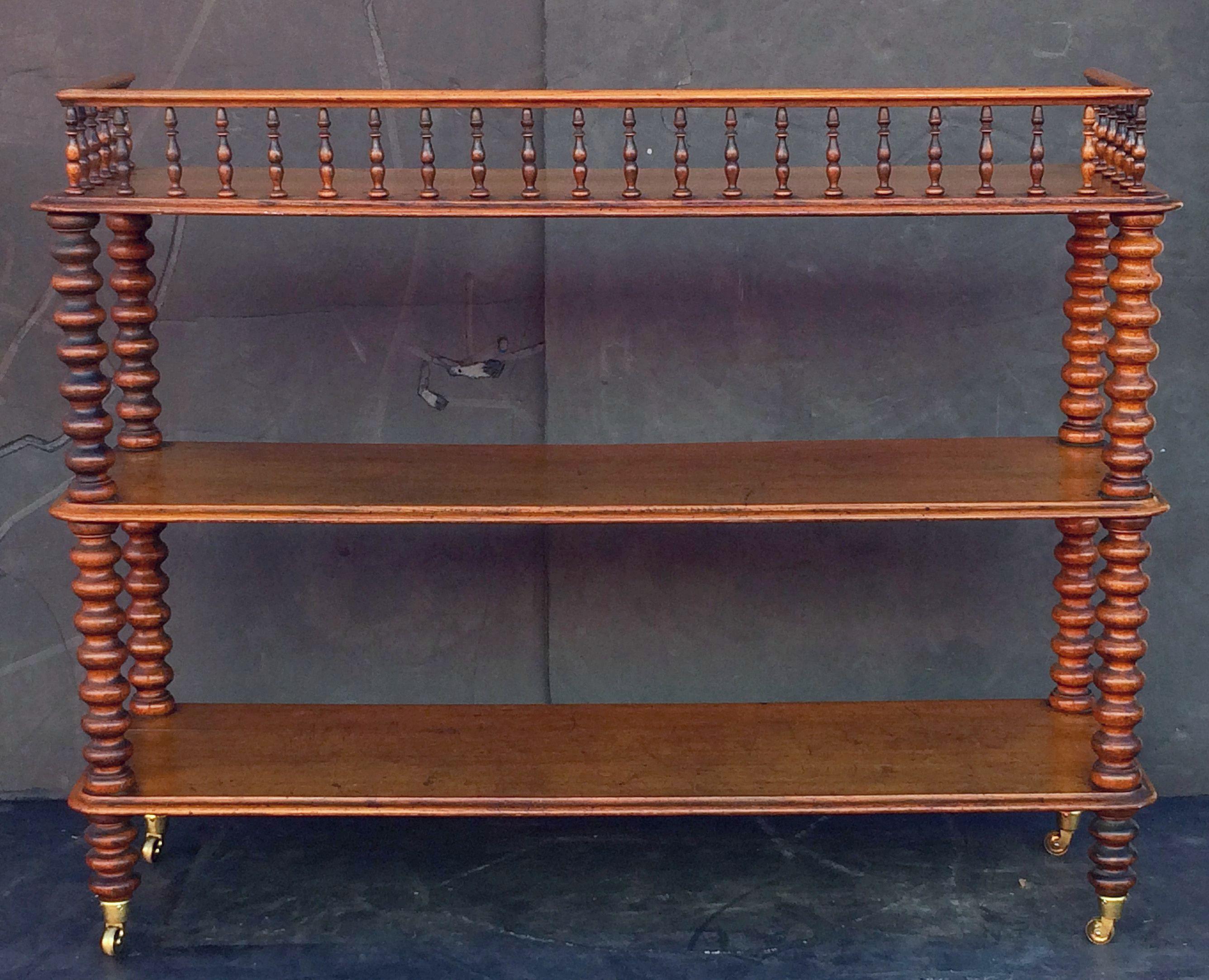 A fine English trolley console server of oak, featuring three tiers with edge-moulded tops, the top tier with back gallery frieze of turned spindles with railing, each tier adjoined to four bobbin turned column supports, set upon rolling brass